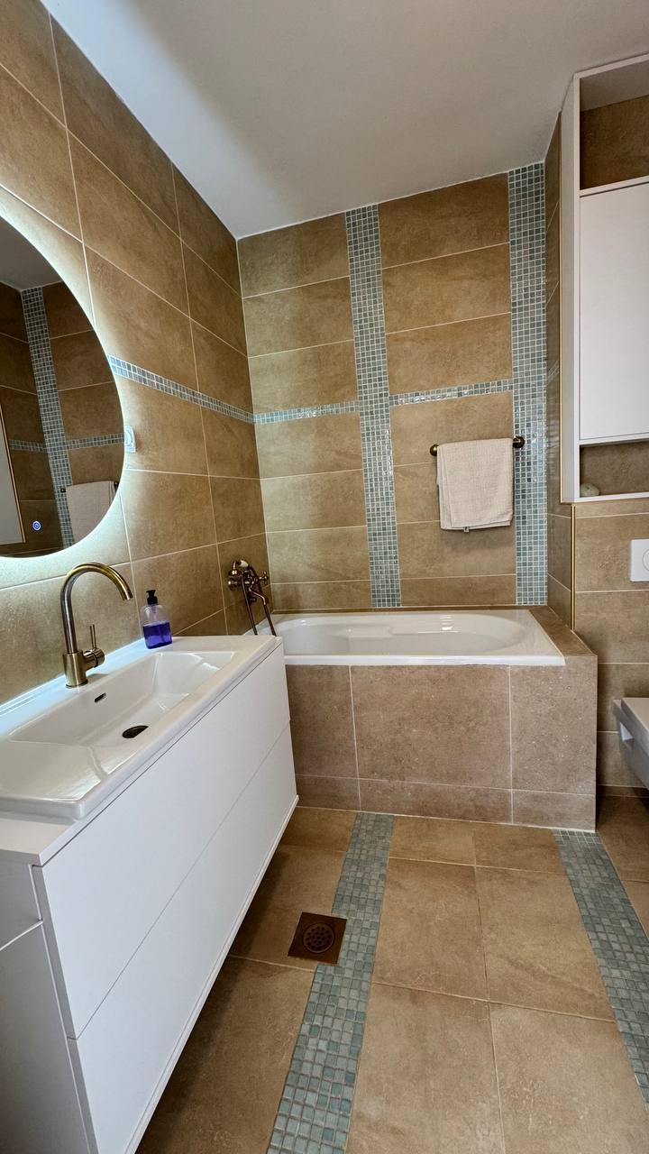 Modern bathroom in an apartment in Budva, Montenegro: white furniture, beige tiles, and gold-tone faucets.