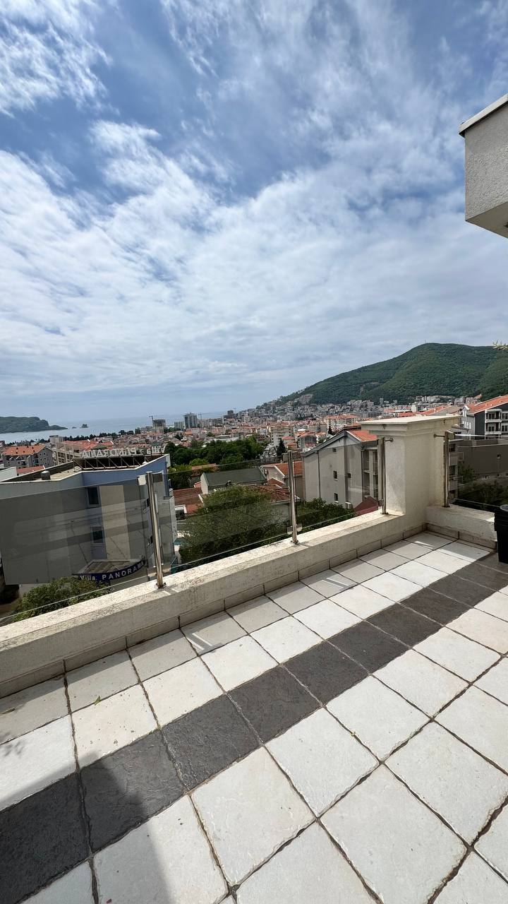 Spacious terrace with panoramic views of the sea and mountains in Budva, Montenegro. Tiled flooring, glass railing.