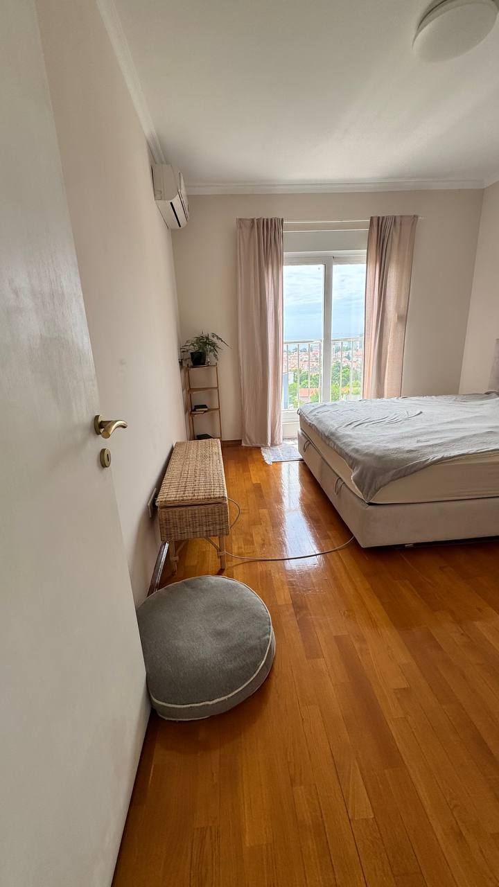 Cozy bedroom with a double bed and parquet flooring in an apartment in Budva, Montenegro, with access to the balcony and city view.