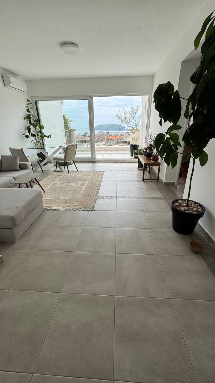 Living room in an apartment in Budva, Montenegro: panoramic windows with sea views, light tile flooring, and modern furniture.