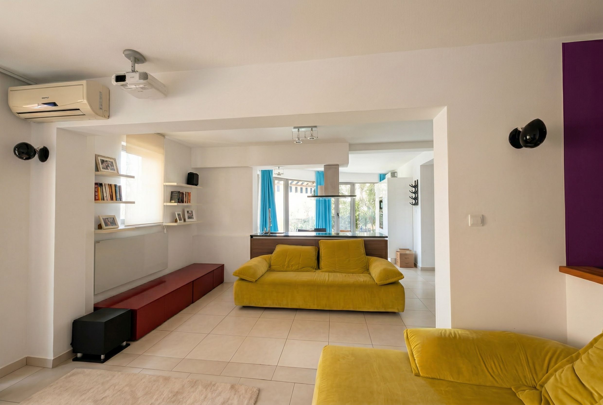 Living room with a yellow sofa and kitchen in an apartment in Bečići, Montenegro: modern interior with a projector and air conditioner.