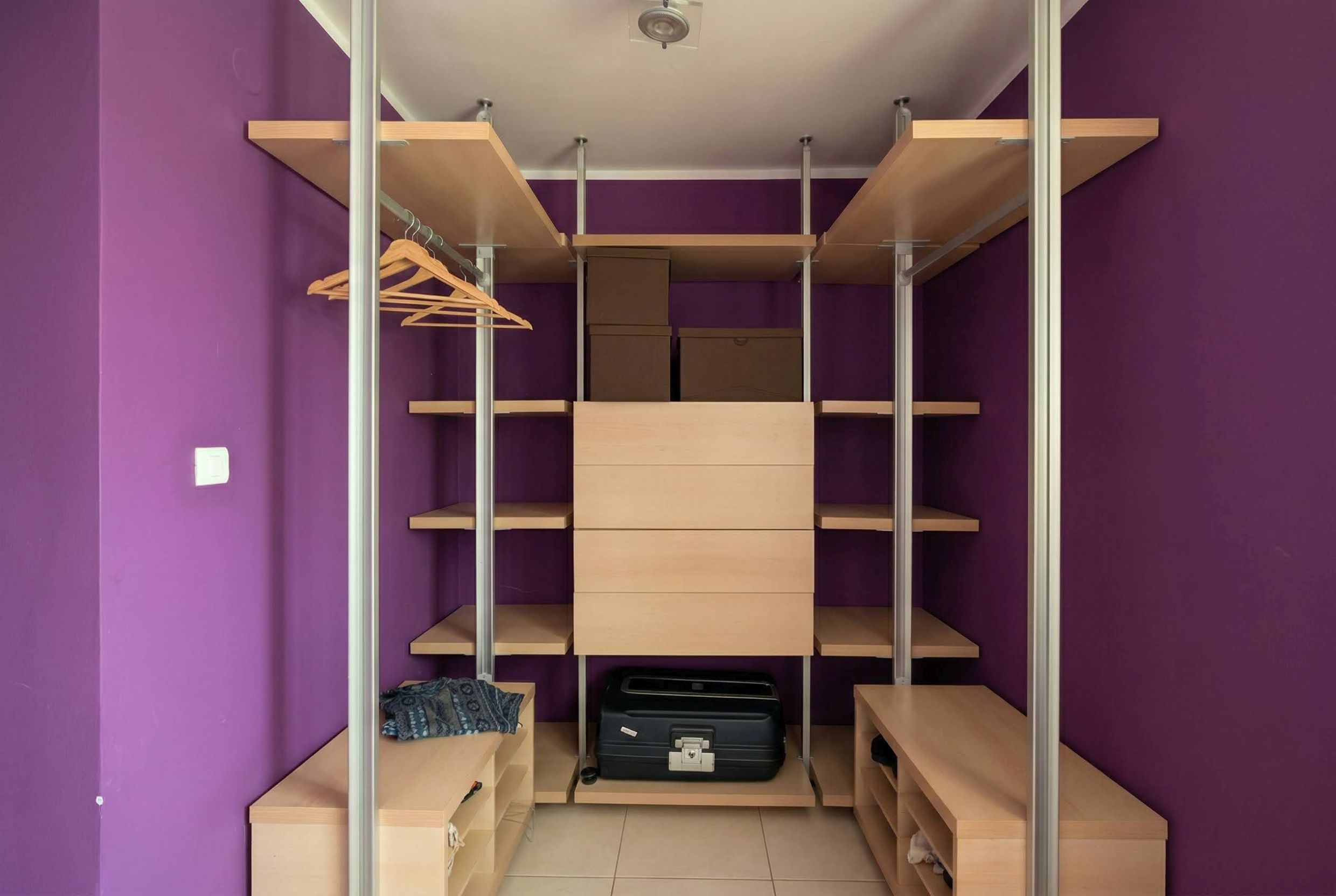 Spacious walk-in closet with wooden shelves and purple walls in an apartment, Becici, Montenegro.