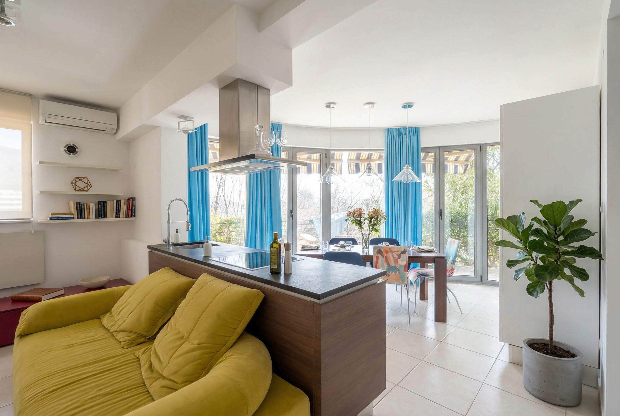 Modern living room with kitchen in an apartment in Becici, Montenegro: yellow sofa, dining area, and panoramic windows.