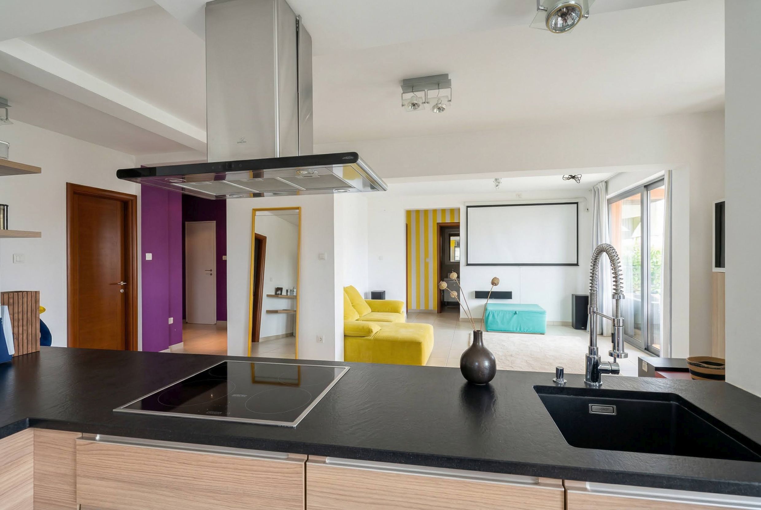 Modern kitchen-living room in an apartment in Bečići, Montenegro: black countertop, bright furniture, and a projector for movies.
