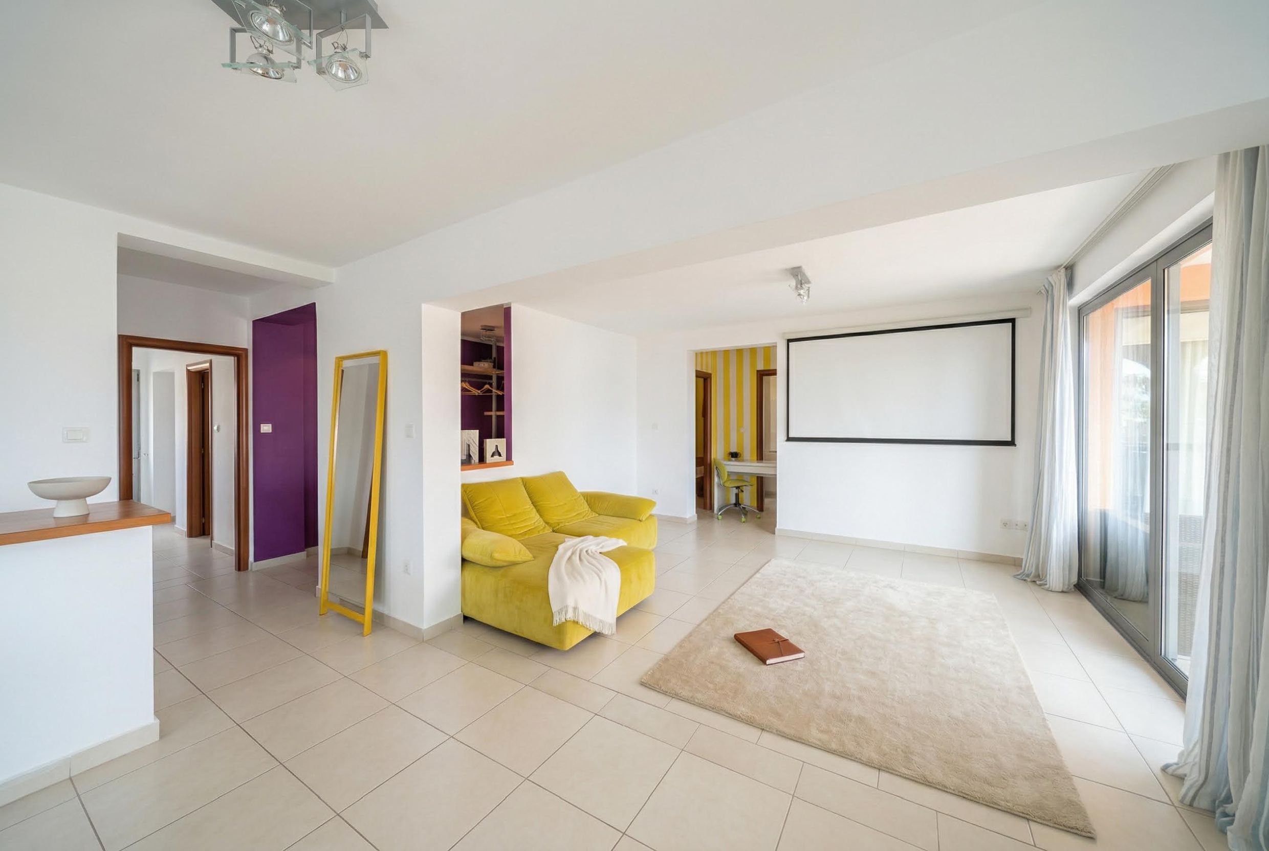 Bright living room with a yellow sofa and projector in an apartment, Becici, Montenegro. Modern interior with a panoramic window.
