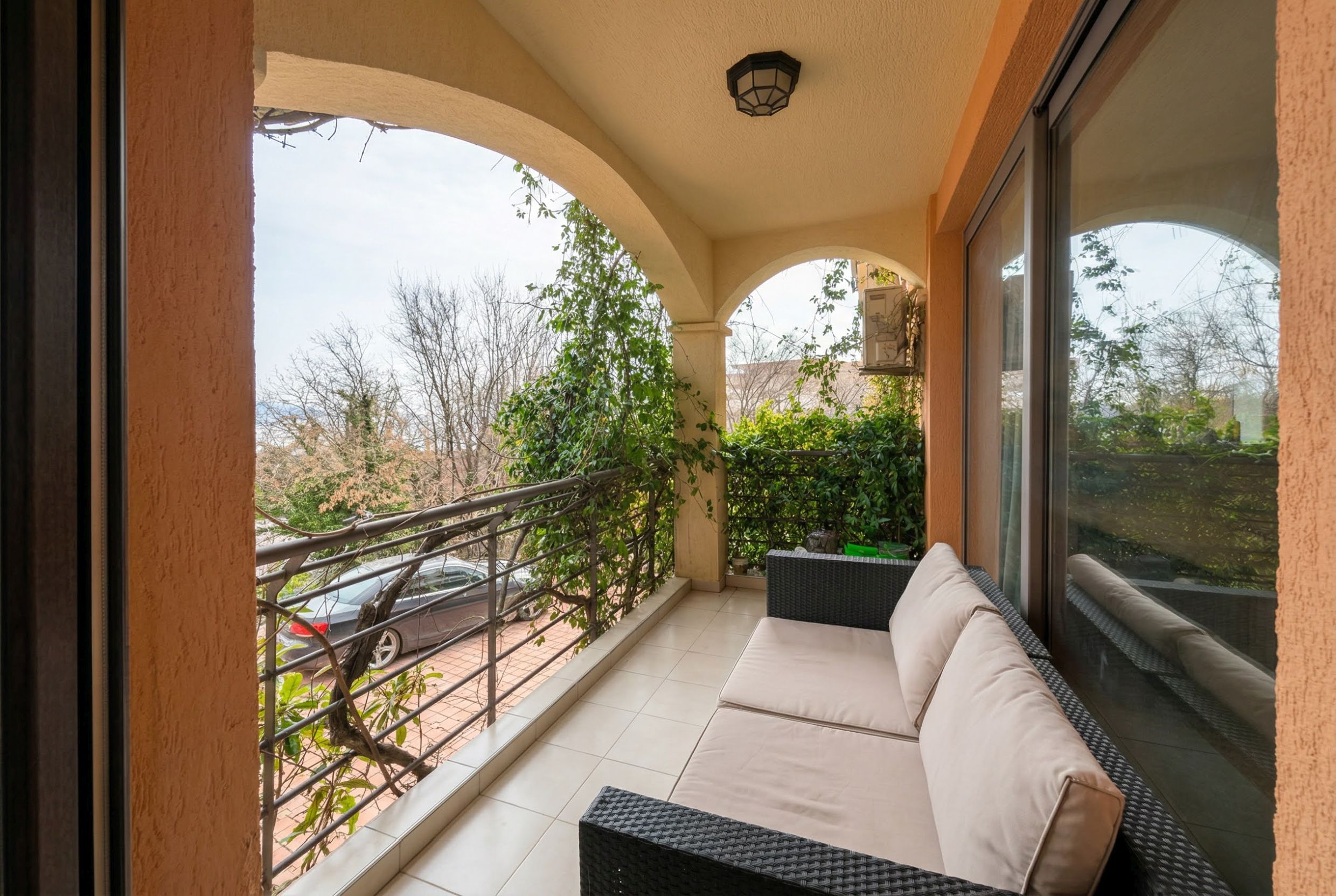Cozy balcony with wicker furniture in an apartment in Bečići, Montenegro: view of greenery and arched decorative elements.