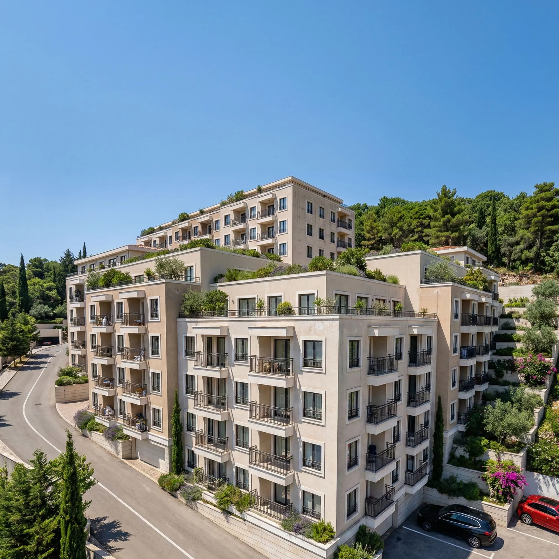 Aerial view of a multi-story residential complex with balconies and terraces surrounded by lush greenery under a clear sky.