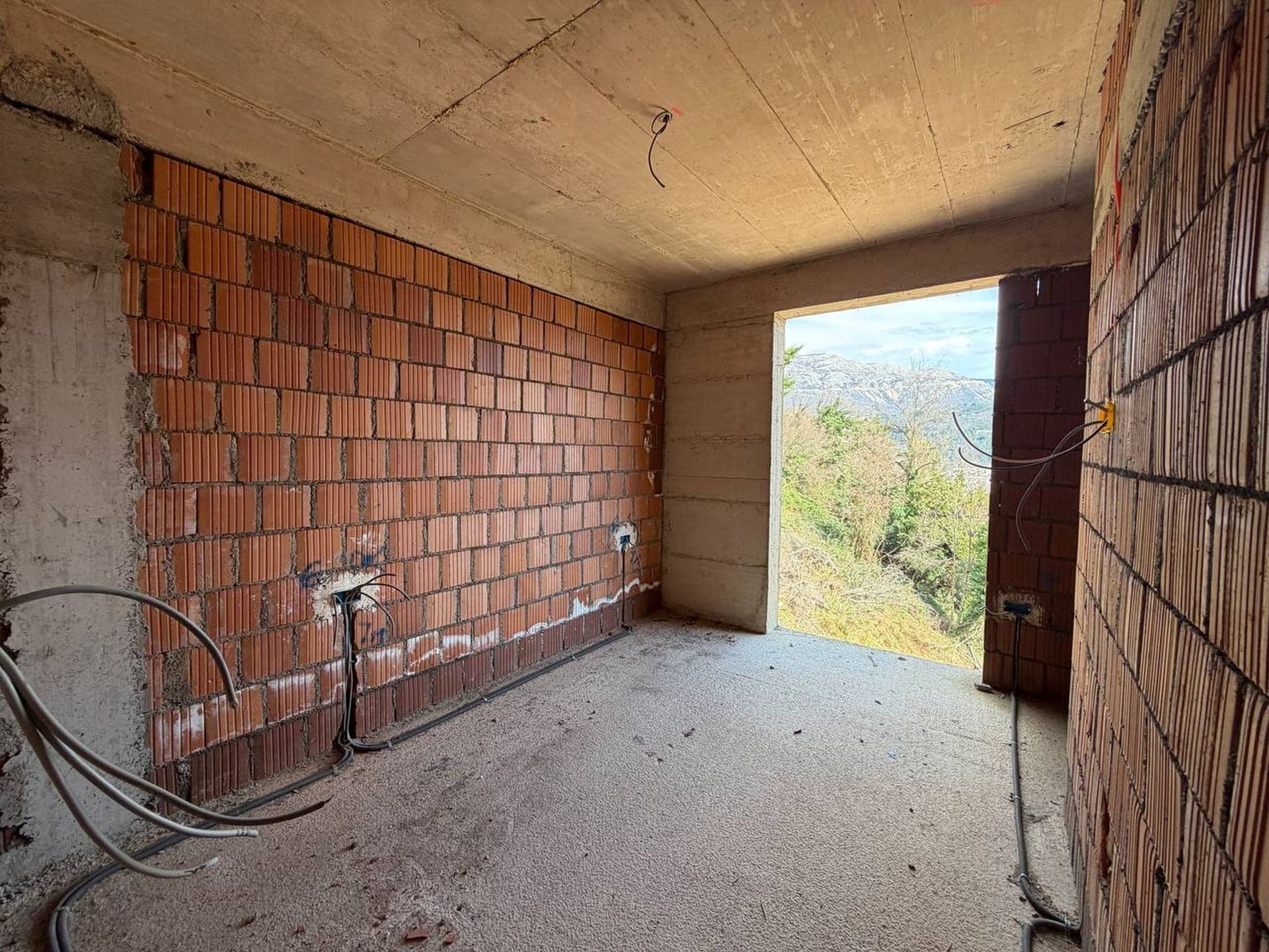 Rough finish of an apartment in a new building in Budva, Montenegro: brick walls, concrete ceiling, and mountain view.