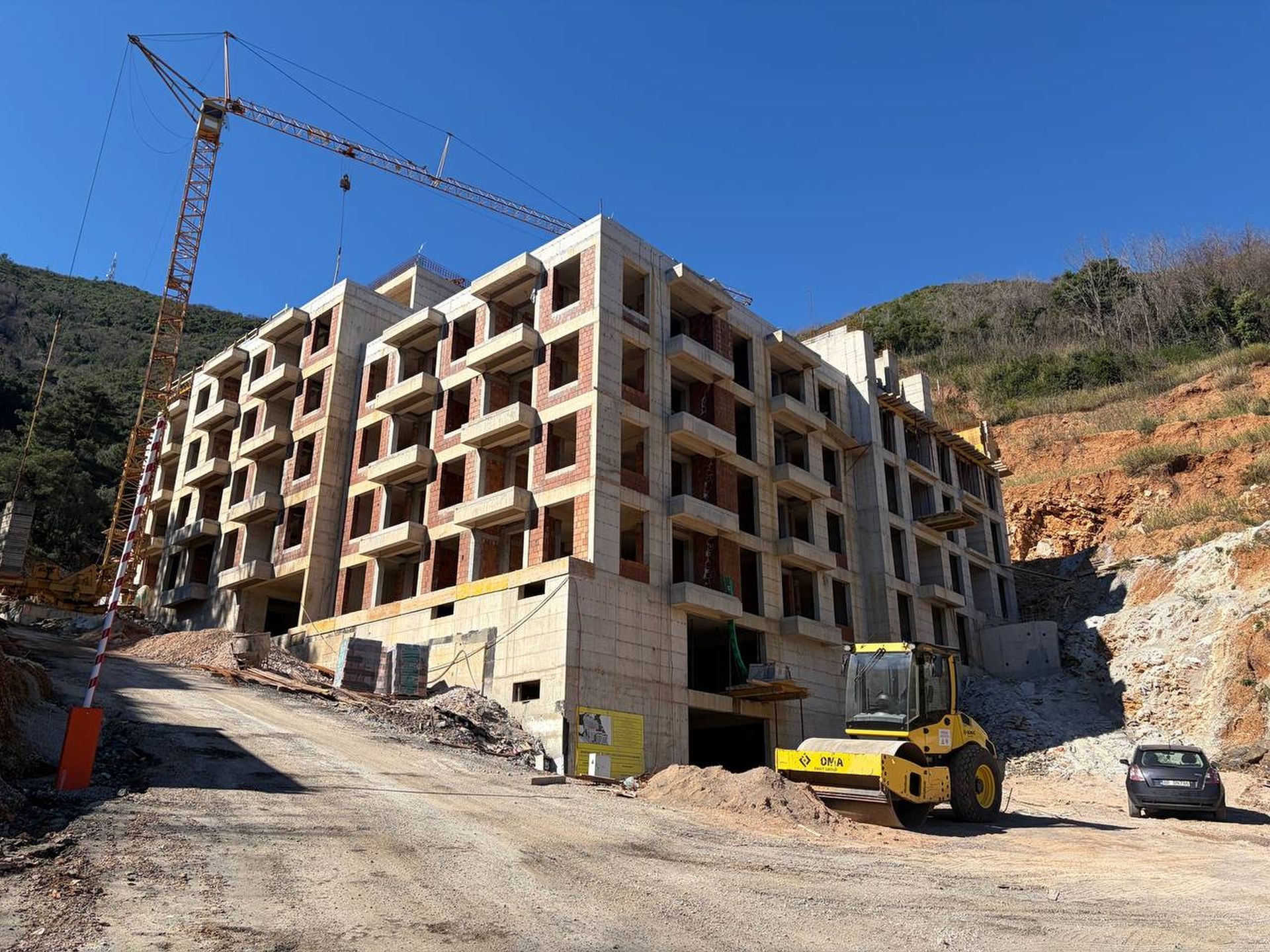 Construction of a residential complex in Budva, Montenegro: a monolithic building with a crane and construction equipment on site.