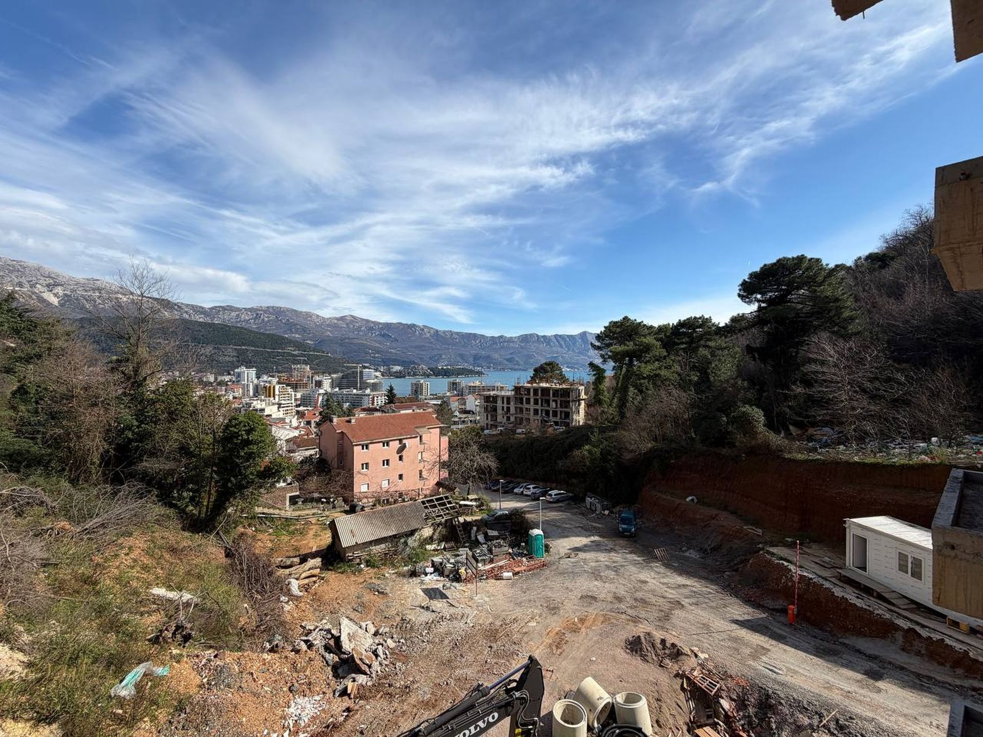 Panoramic view of Budva and the sea from a residential complex under construction in Montenegro, with views of the mountains and the construction site.