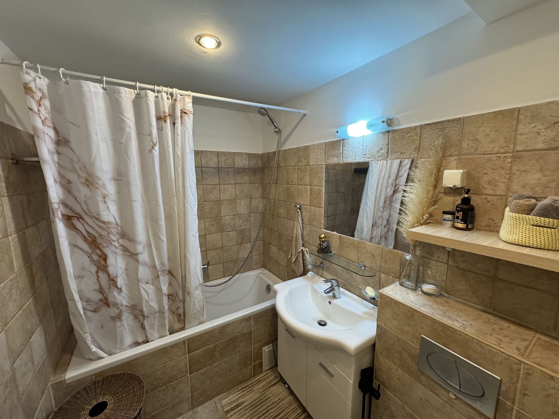 Bathroom in an apartment in Dobrota, Montenegro: white fixtures, beige-toned tiles, and a shower with a curtain.