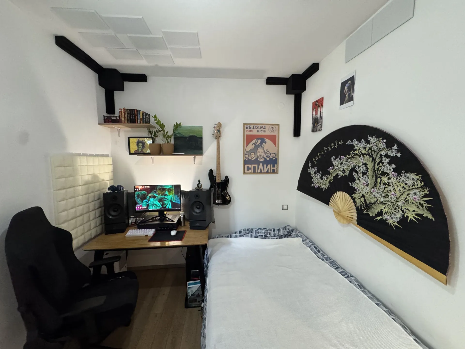 Small bedroom featuring a computer desk, black chair, bass guitar on the wall, and a large decorative fan.