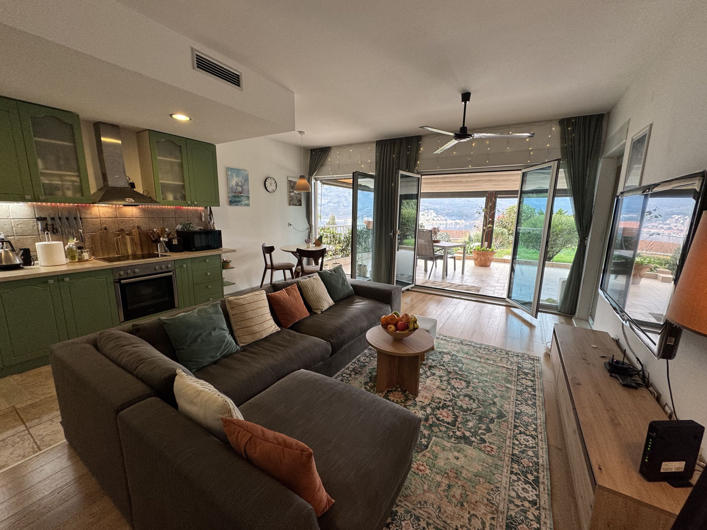 Living room with kitchen in an apartment in Dobrota, Montenegro: corner sofa, access to a terrace with sea and mountain views.