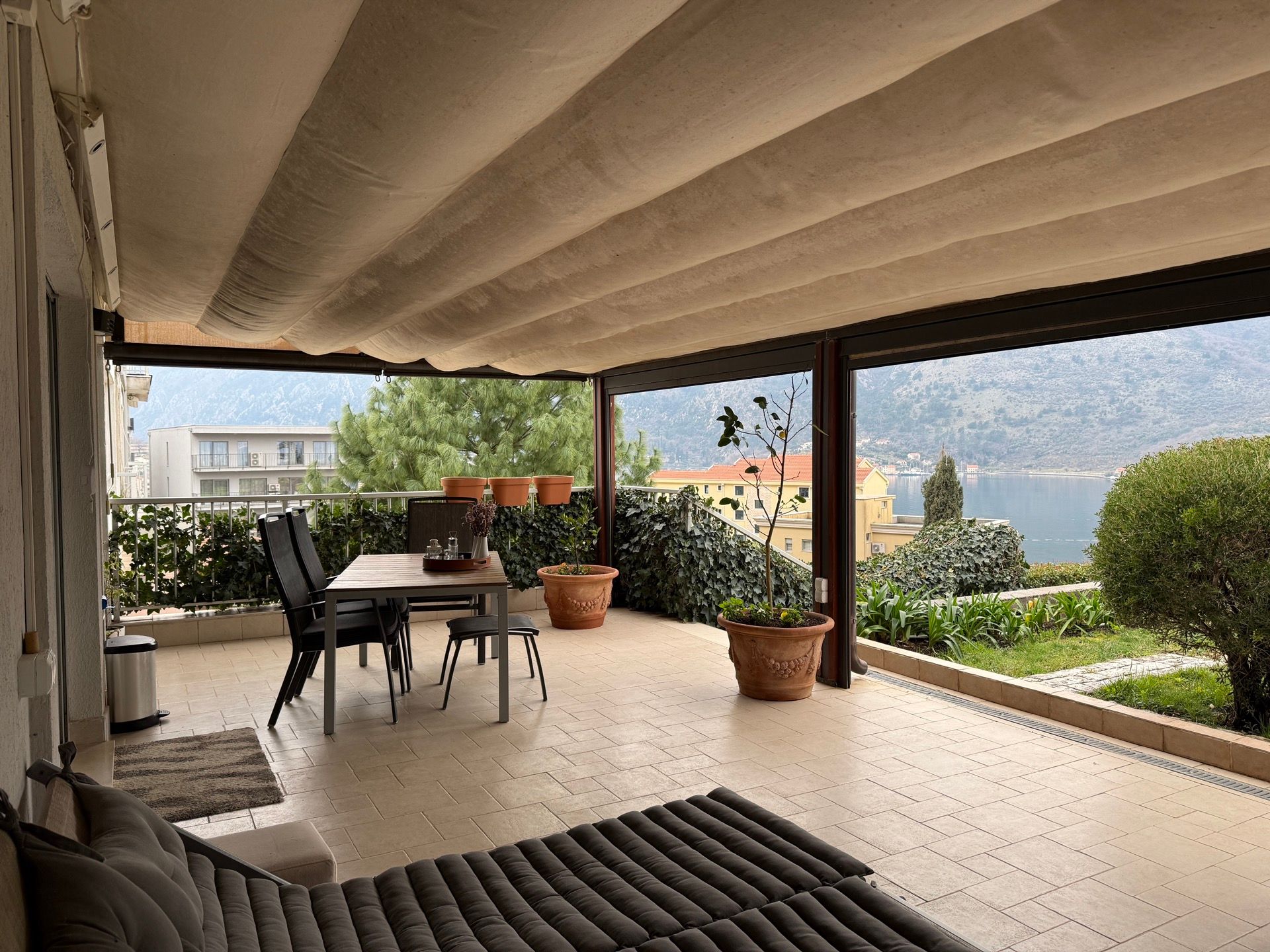 Spacious terrace with dining area and views of Kotor Bay, apartment in Dobrota, Montenegro, awning and furniture.