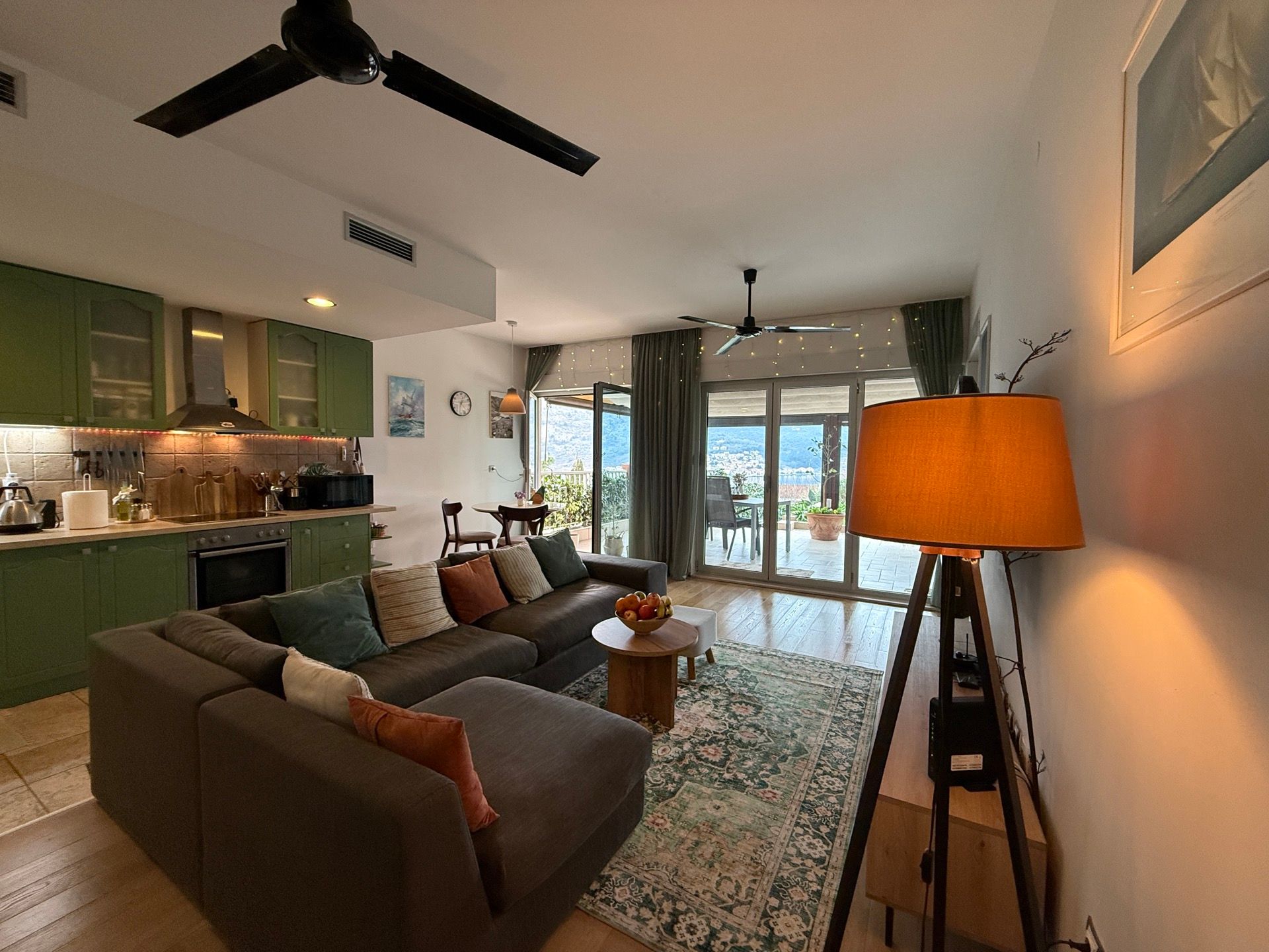 Living room with kitchen in an apartment in Dobrota, Montenegro: corner sofa, green furniture, terrace with sea view.