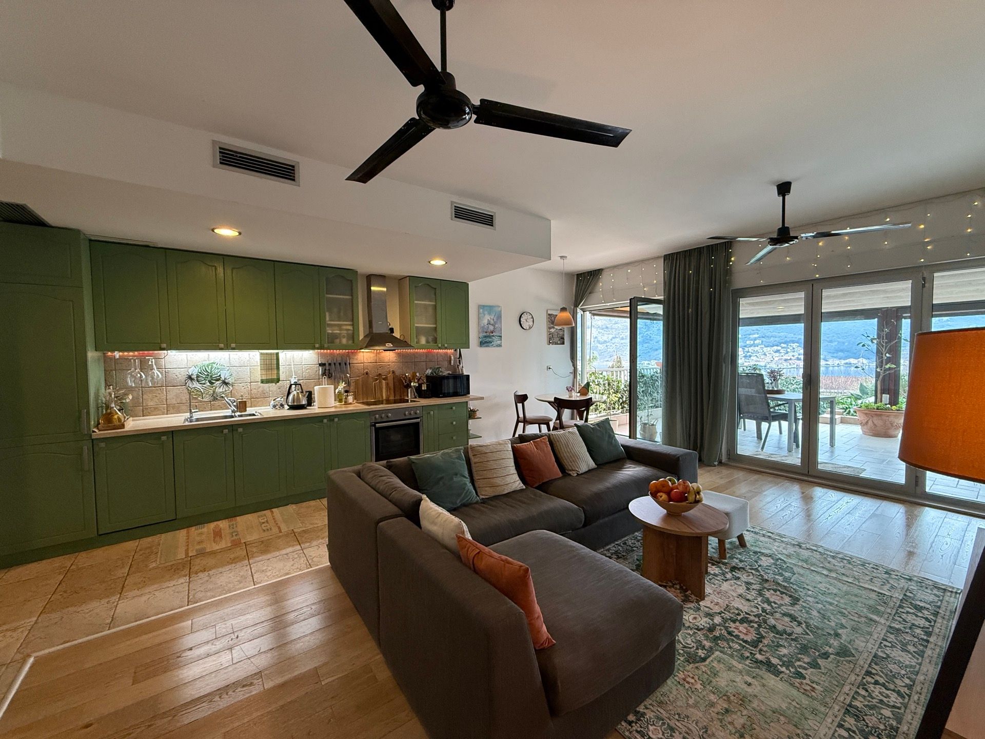 Living room with a green kitchen and a terrace with sea view in an apartment, Dobrota, Montenegro. Modern interior with a sofa.