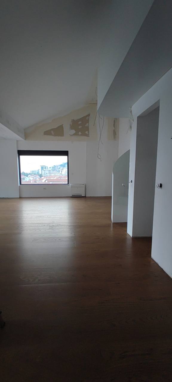 Spacious living room in a penthouse in Budva, Montenegro: light finishes, wooden flooring, and panoramic city views.