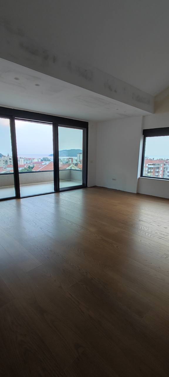 Bright living room in a penthouse in Budva, Montenegro: panoramic windows, sea view, parquet flooring, and terrace access.