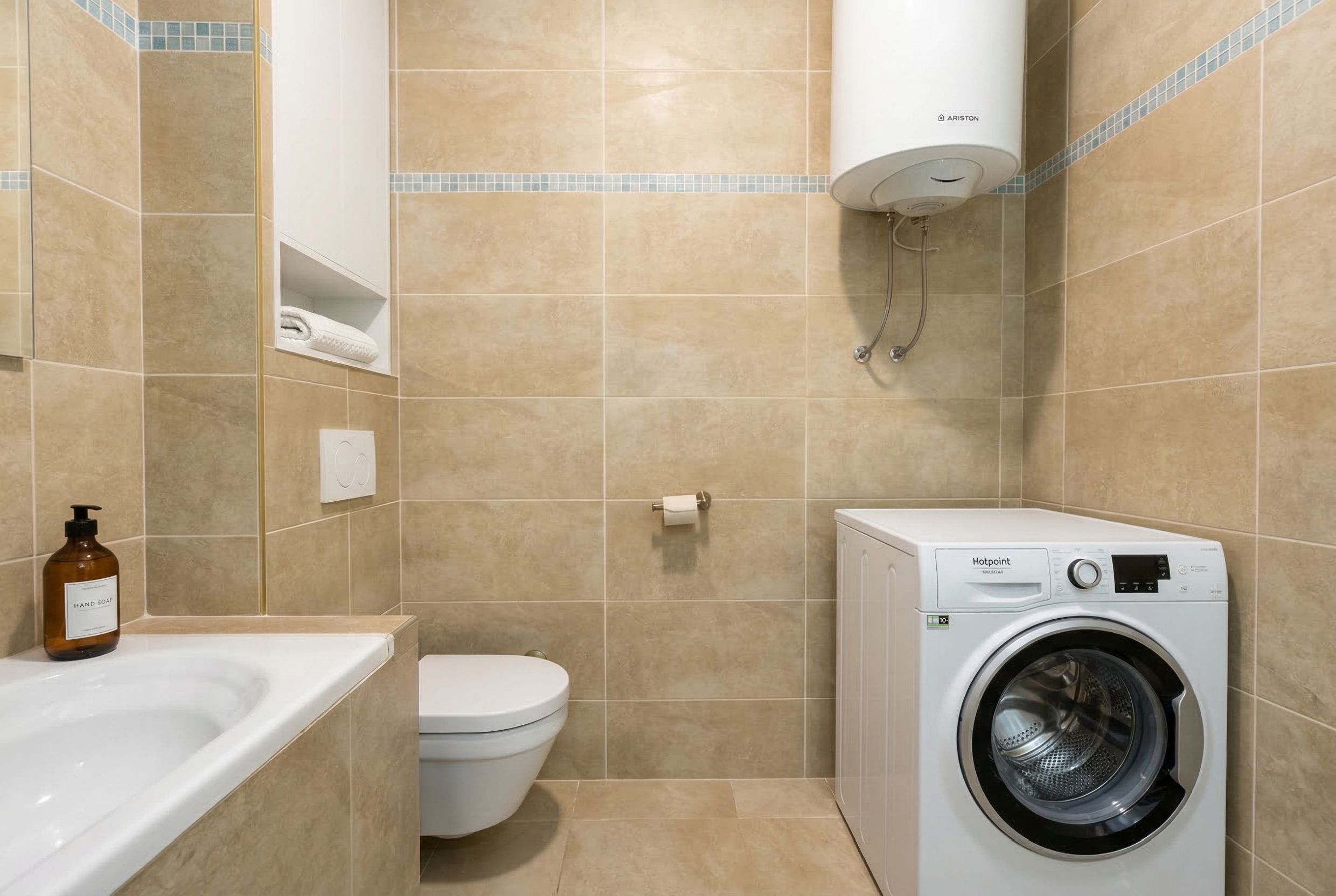 Bathroom in an apartment in Budva, Montenegro: beige tiles, Hotpoint washing machine, Ariston water heater, and plumbing fixtures.