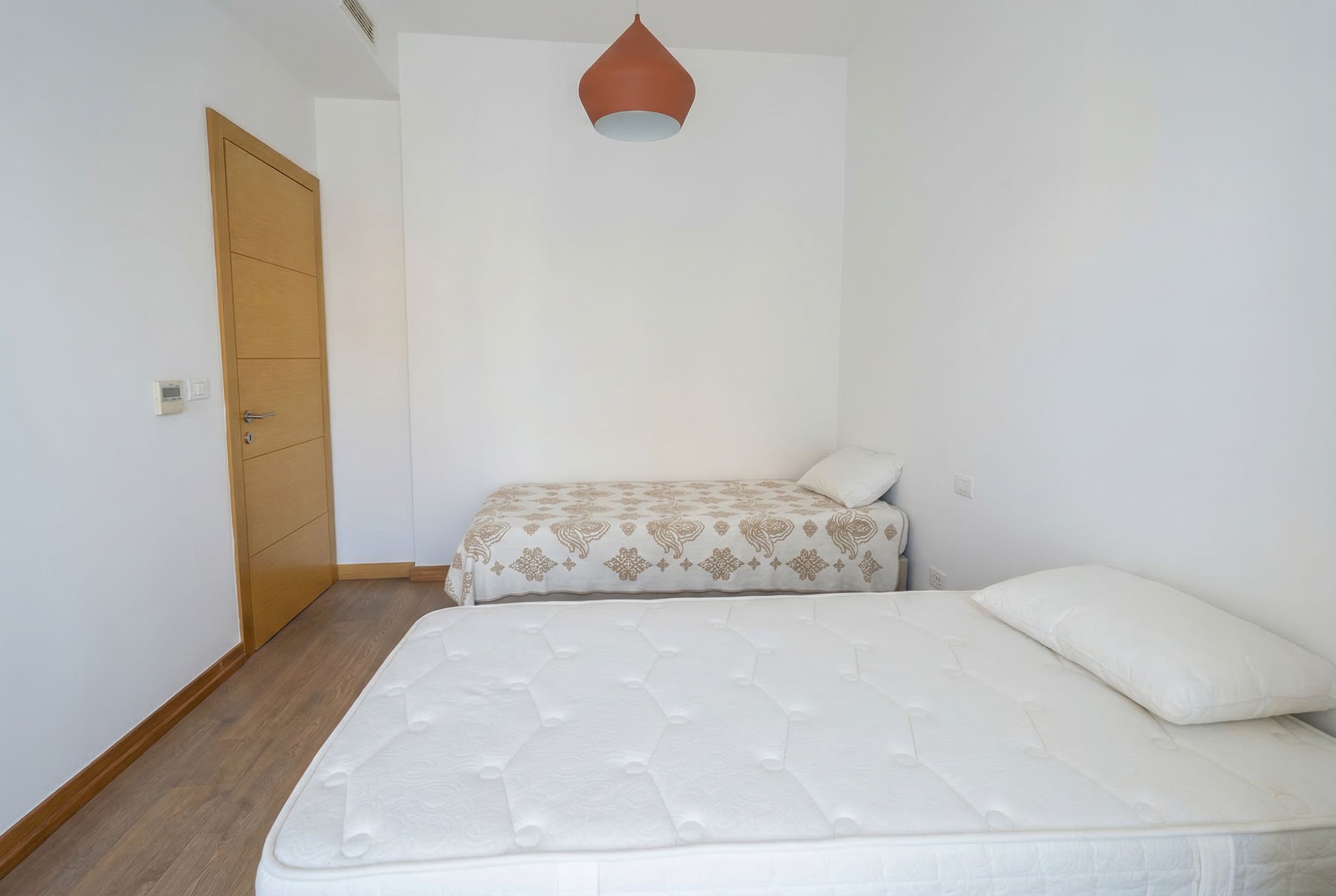 Bright bedroom with two beds, wooden flooring, and modern finishes in an apartment, Budva, Montenegro.