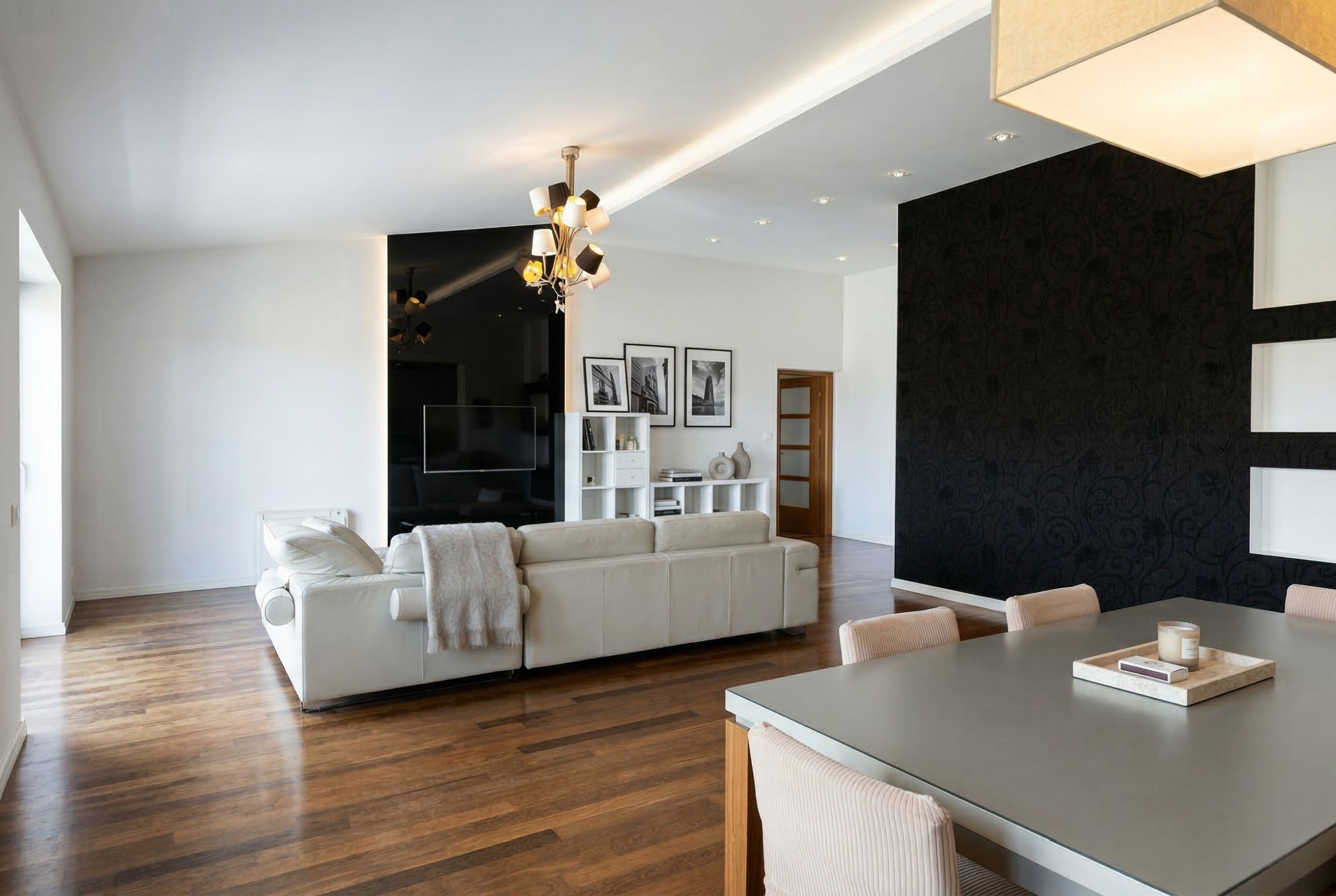Modern living room in a penthouse in Kamenovo, Montenegro: white leather sofa, black wall decor, and dining area.