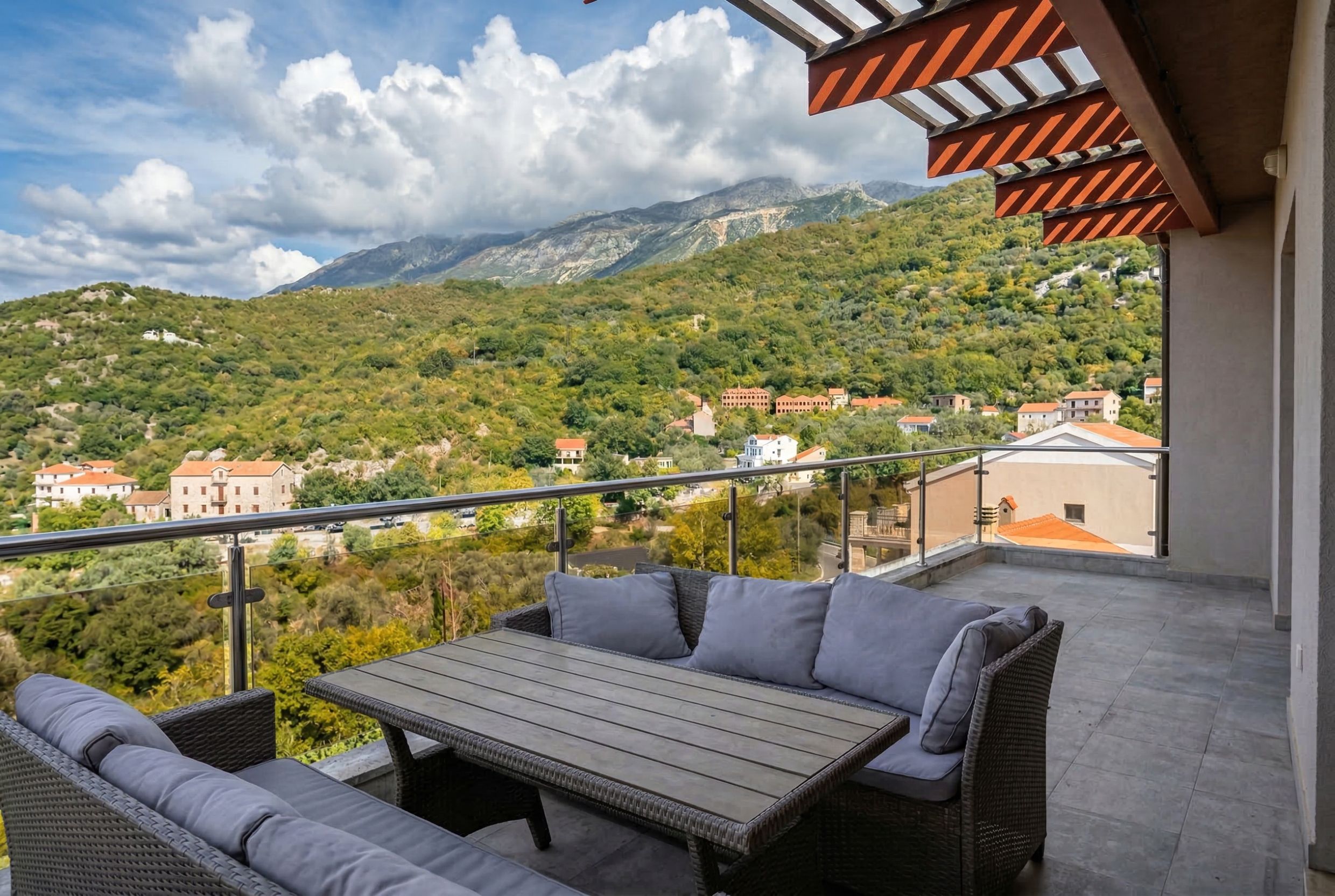 Penthouse terrace in Kamenovo, Montenegro: wicker furniture, panoramic view of the mountains and green hills.