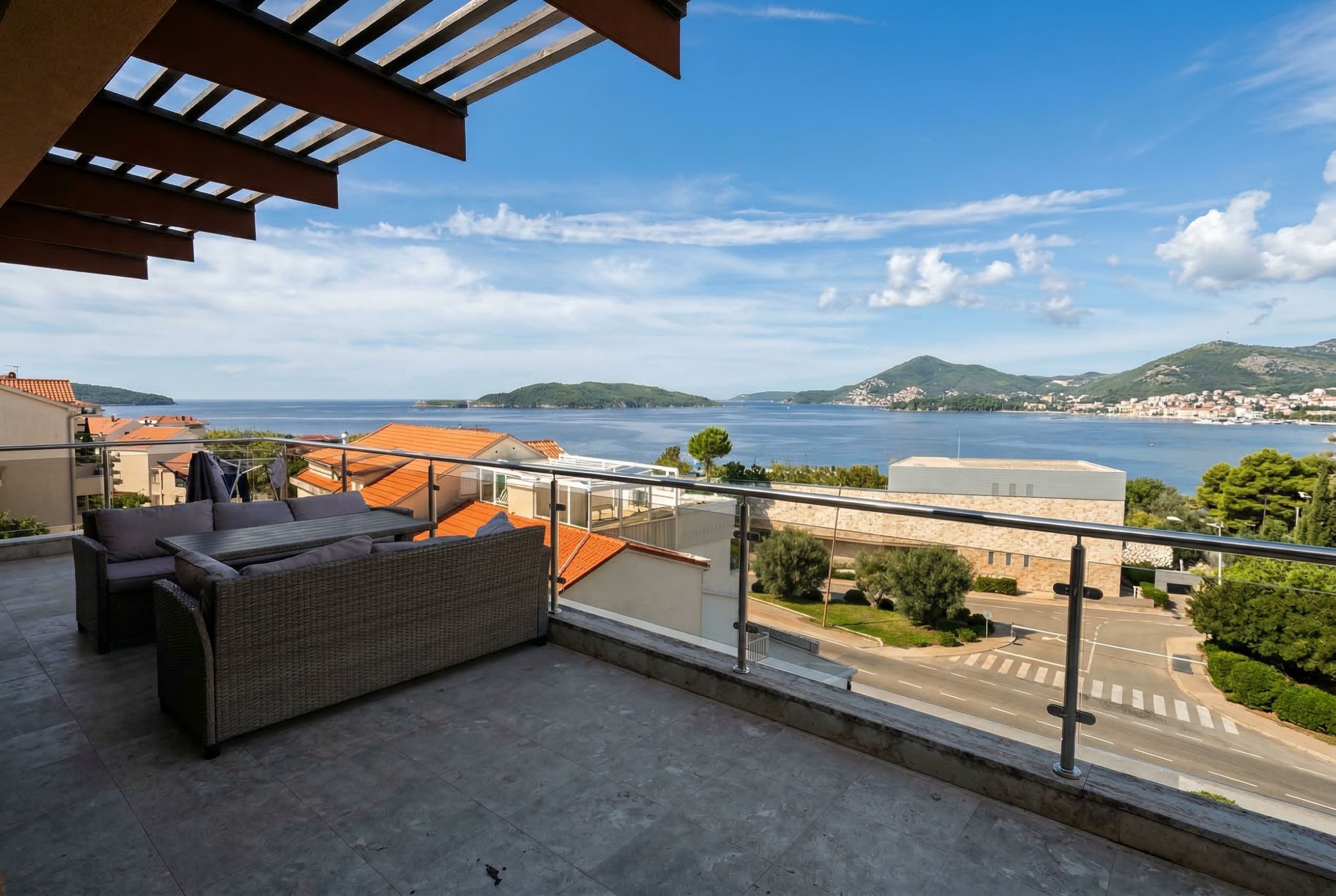 Penthouse terrace in Kamenovo, Montenegro: wicker furniture, panoramic sea and island views, modern railing.