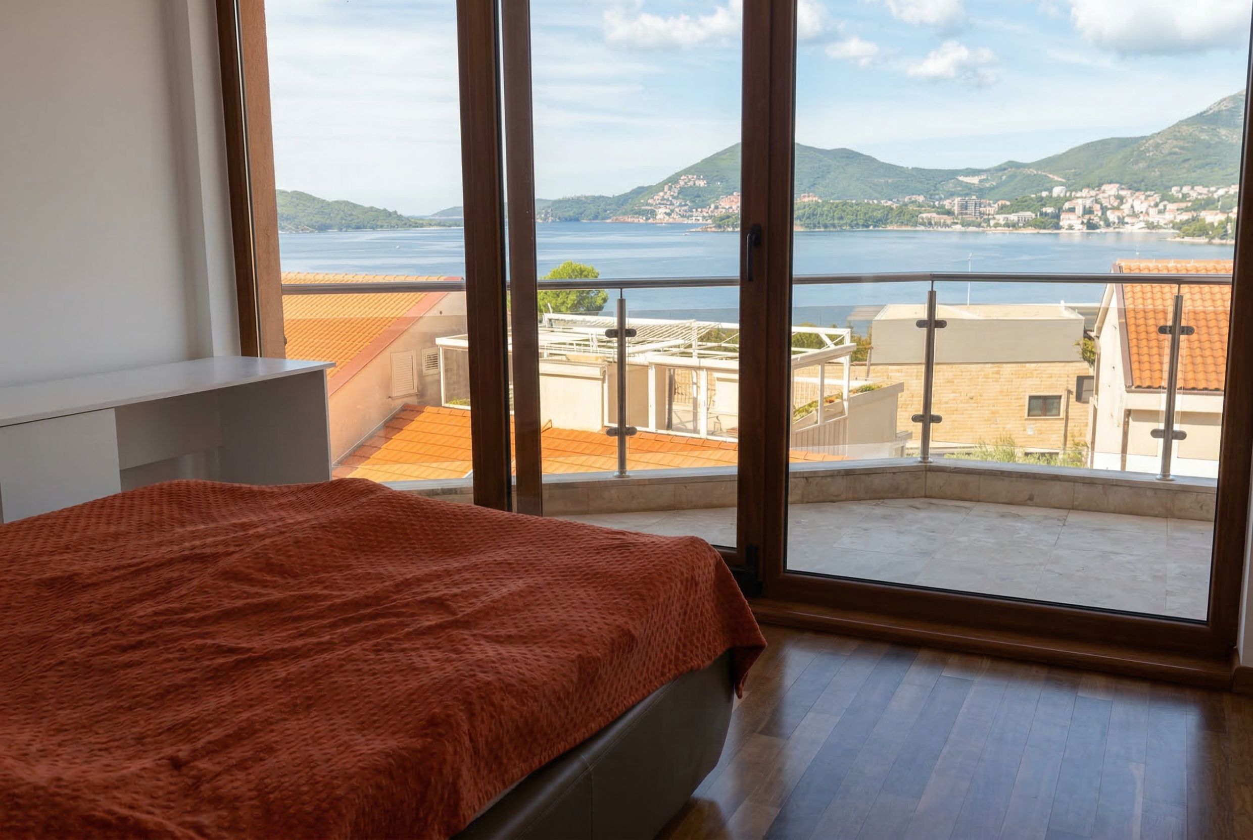 Penthouse bedroom in Kamenovo, Montenegro: panoramic sea view, terrace, double bed, and parquet flooring.