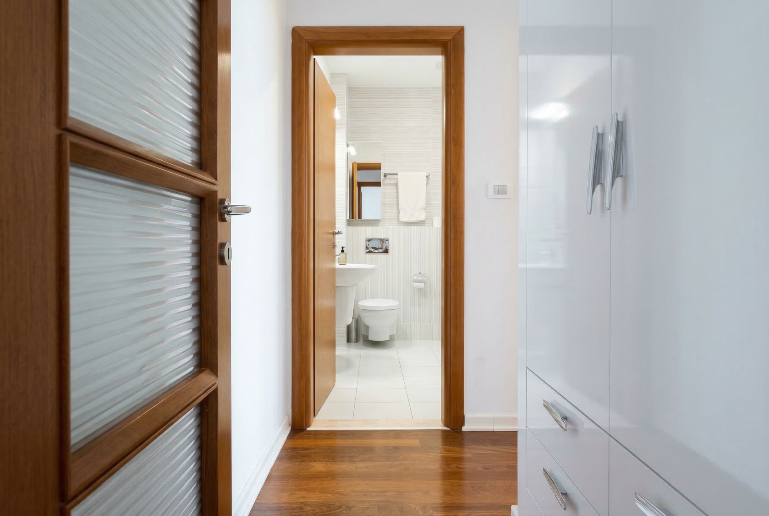 View from the hallway into a modern bathroom in a penthouse, Kamenovo, Montenegro: light tiles and wooden doors.