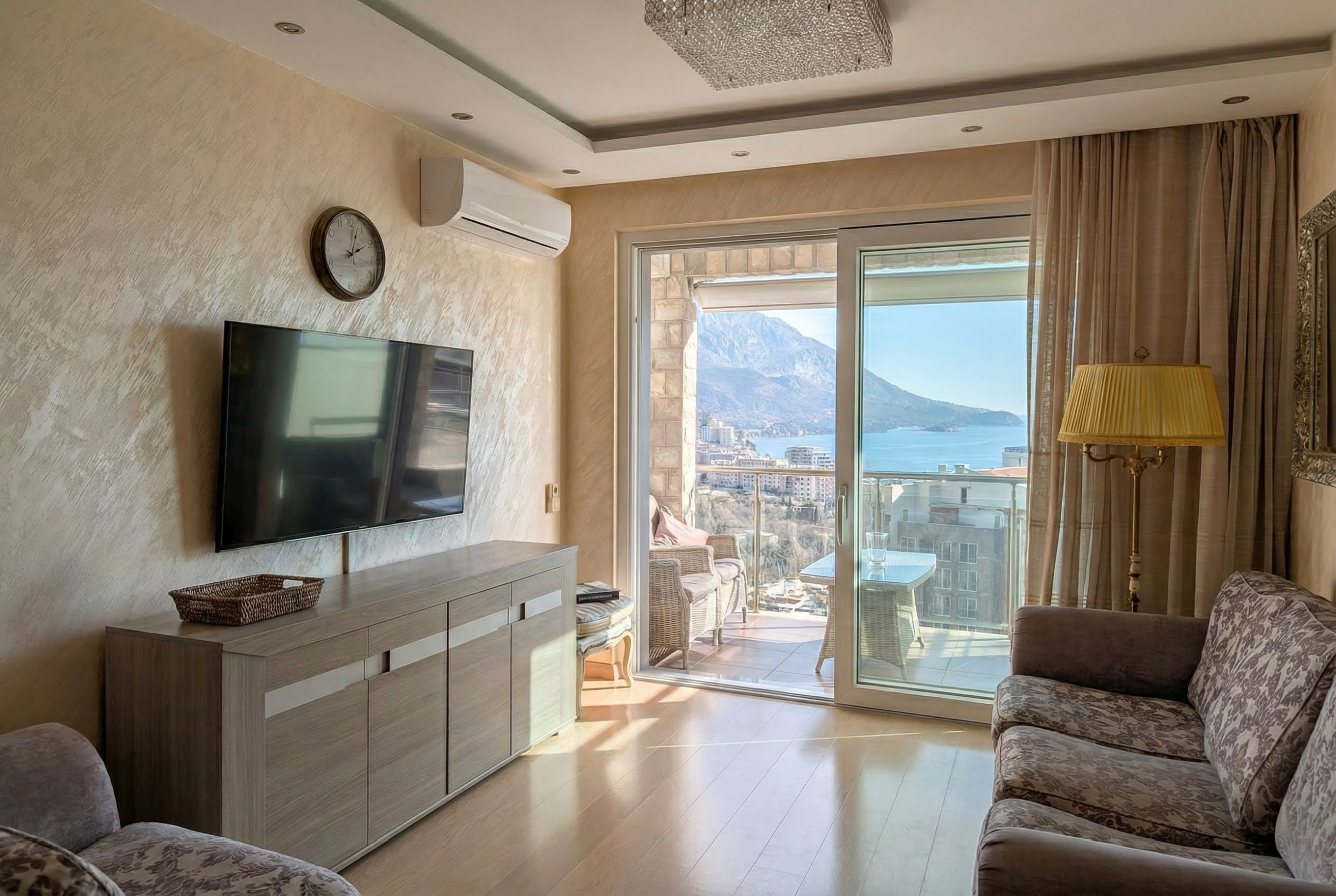 Living room in an apartment in Bečići, Montenegro: modern furniture, TV, panoramic sea and mountain views from the terrace.