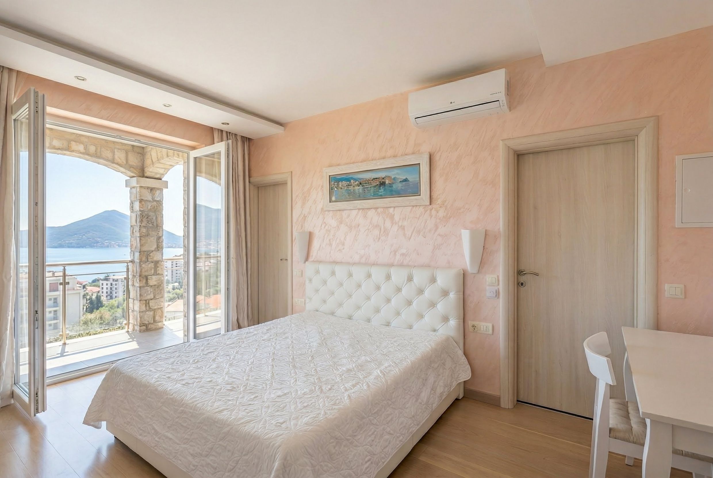 Bedroom in an apartment in Bečići, Montenegro: white bed, terrace with panoramic sea and mountain views, bright interior.