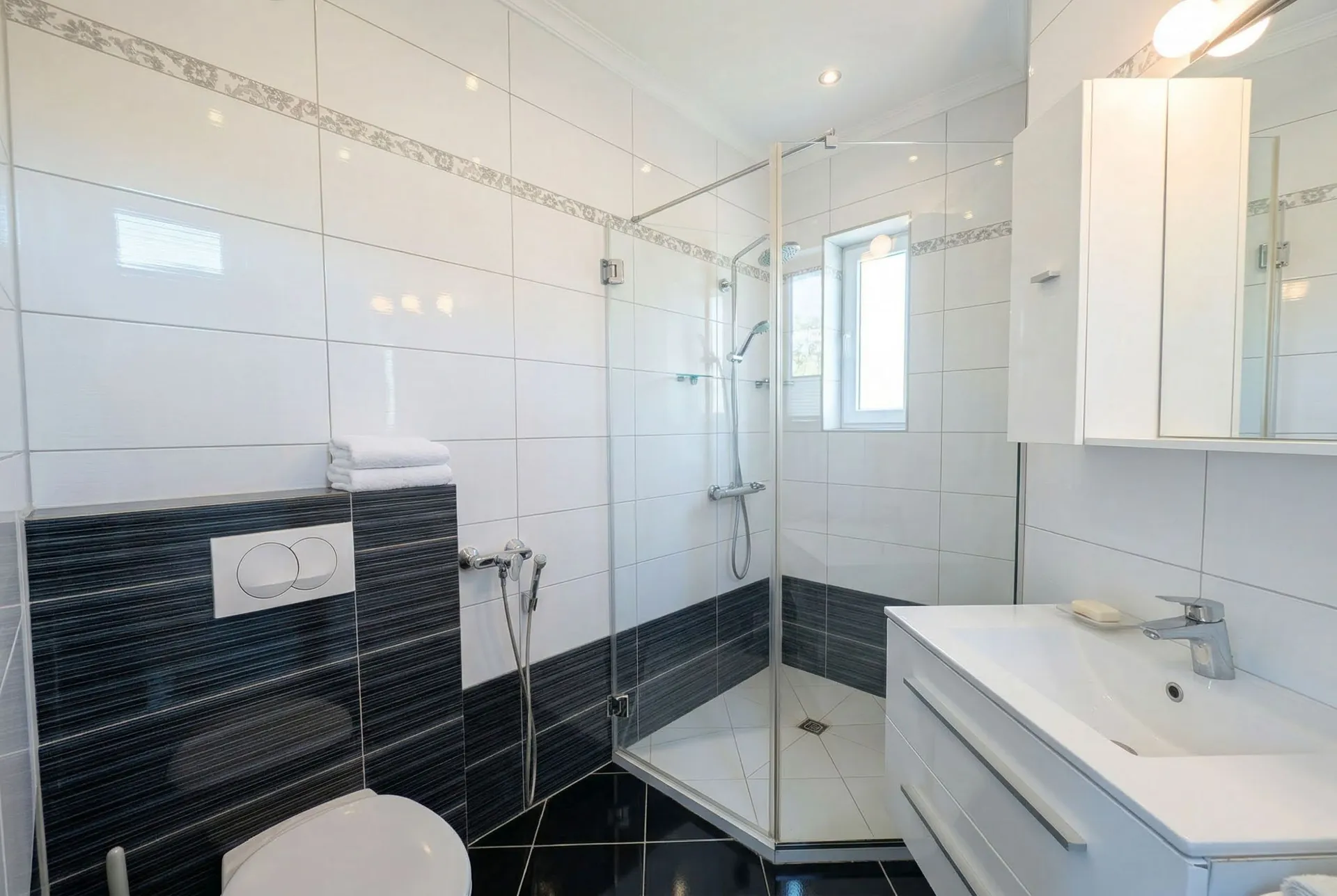 Modern bathroom featuring black and white tiles, a glass shower enclosure, white vanity sink, and a wall-mounted toilet.