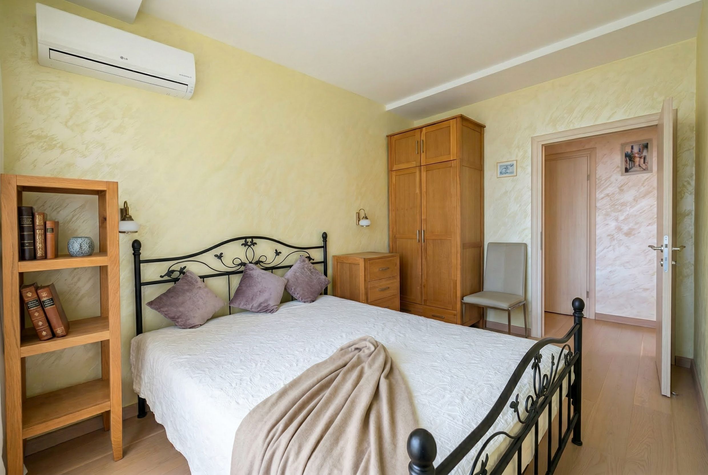 Bedroom in an apartment in Bečići, Montenegro: wrought-iron bed, wooden wardrobe, light walls, and air conditioning.