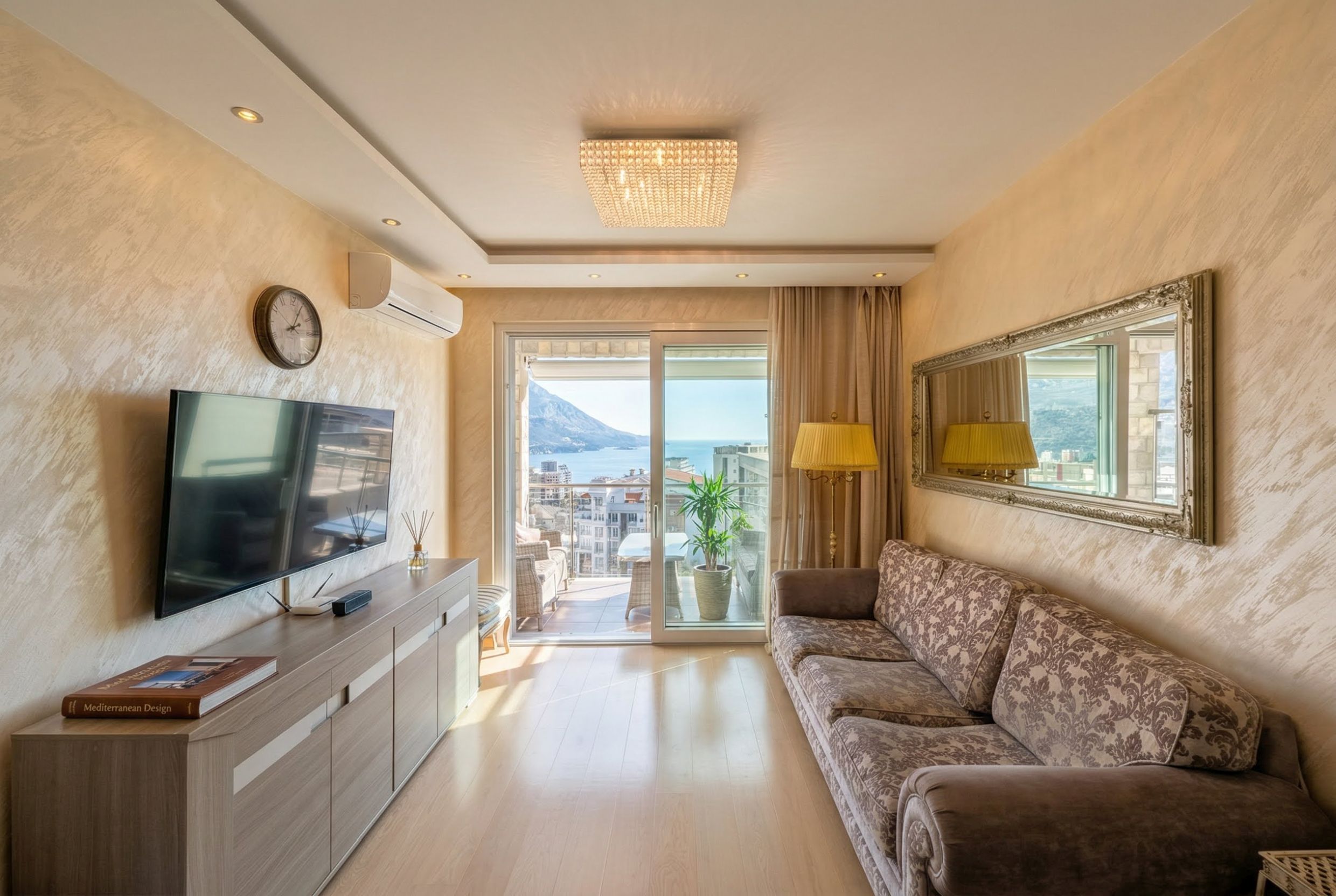 Living room in an apartment in Bečići, Montenegro: a soft sofa, TV area, and panoramic sea and mountain views from the terrace.
