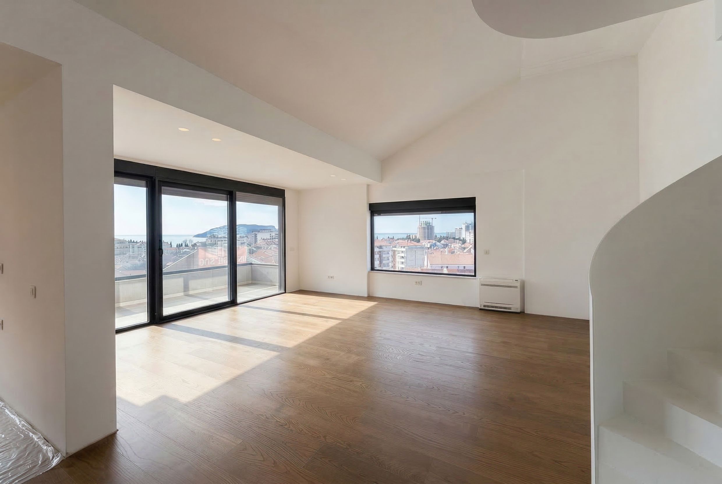 Bright living room in a Budva penthouse, Montenegro: panoramic windows, sea view, wooden flooring, and staircase.