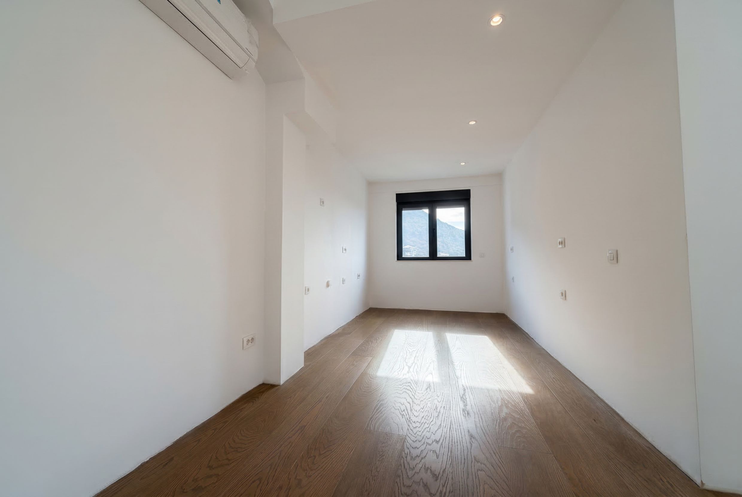 Bright empty bedroom with parquet flooring and mountain views in a penthouse, Budva, Montenegro. Modern finishes and air conditioning.