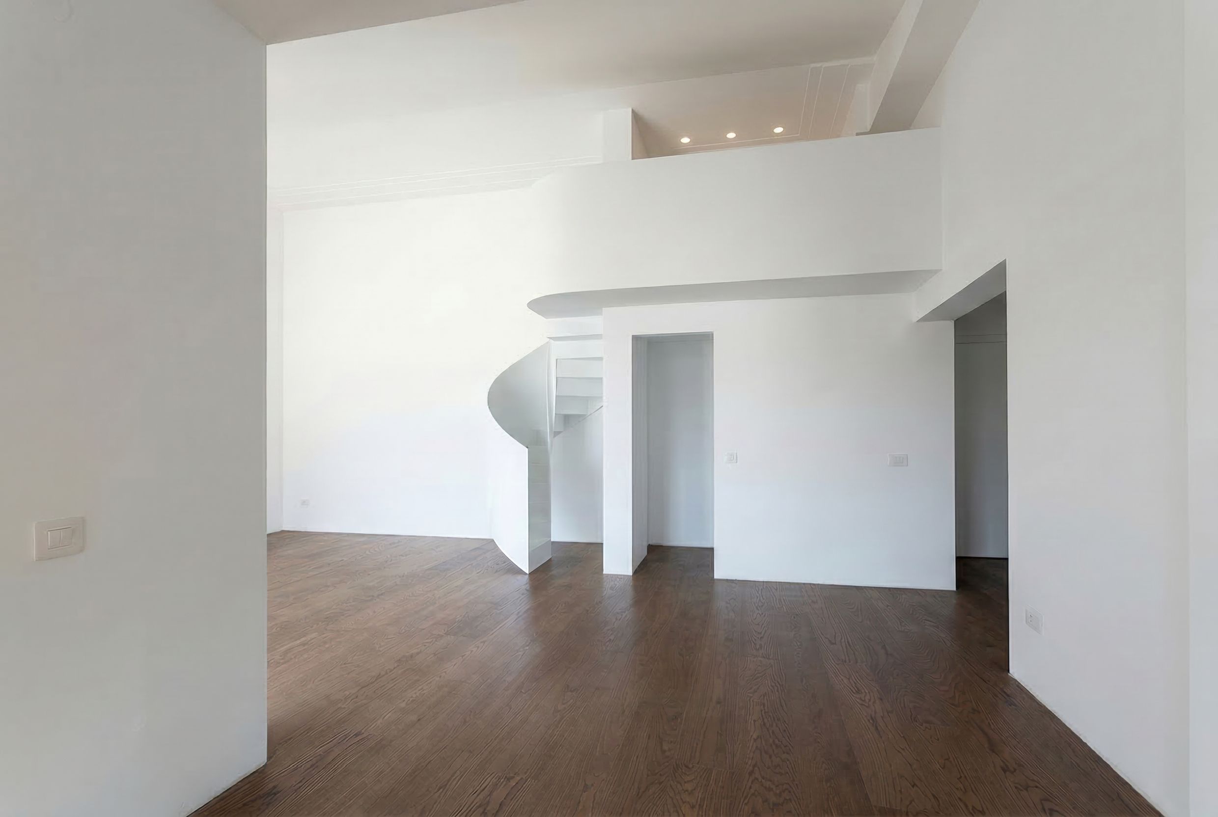 Interior of a duplex living room in a penthouse in Budva, Montenegro: white walls, spiral staircase, and parquet flooring.
