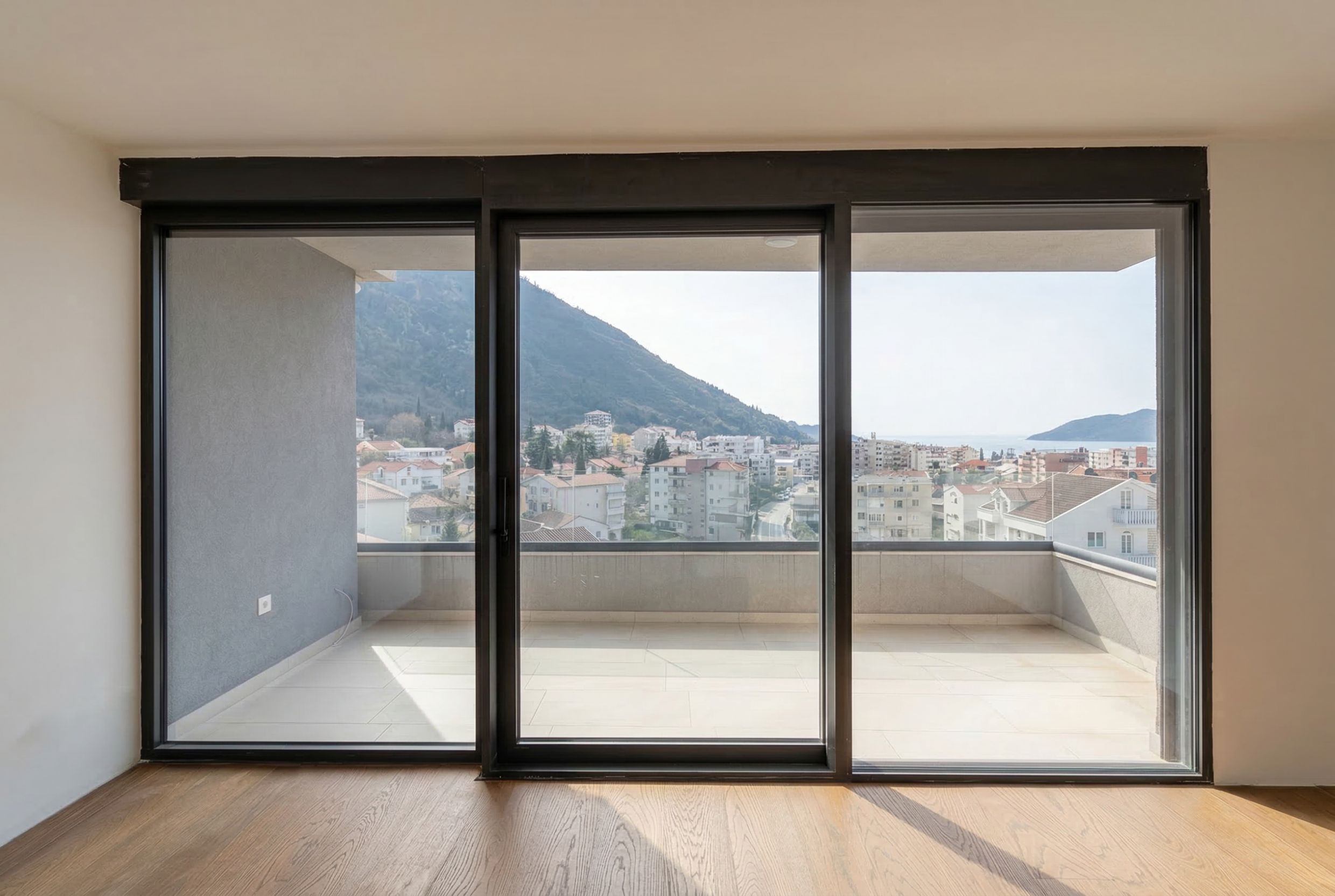 Panoramic windows in a penthouse living room in Budva, Montenegro, with access to a spacious terrace and views of the mountains and the sea.