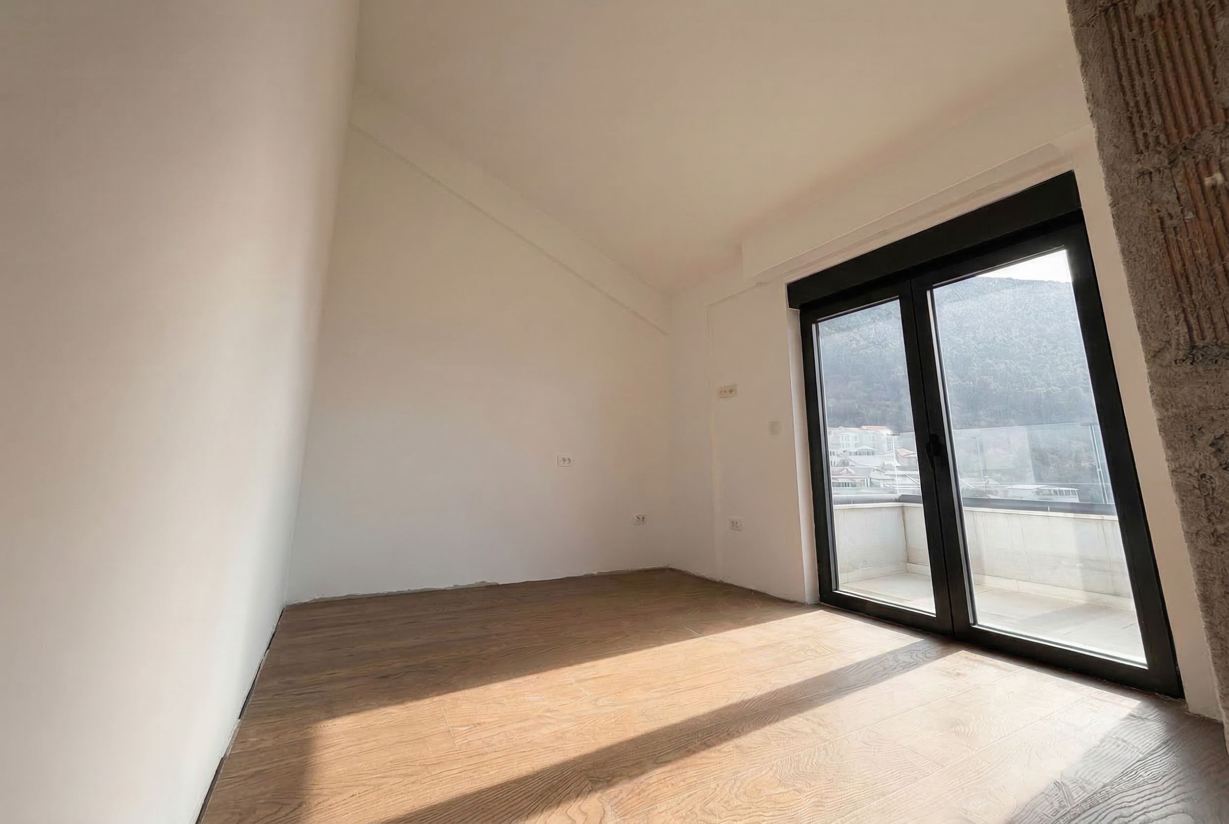 Bright bedroom in a penthouse in Budva, Montenegro: panoramic window, access to the terrace, white-box finish, mountain view.