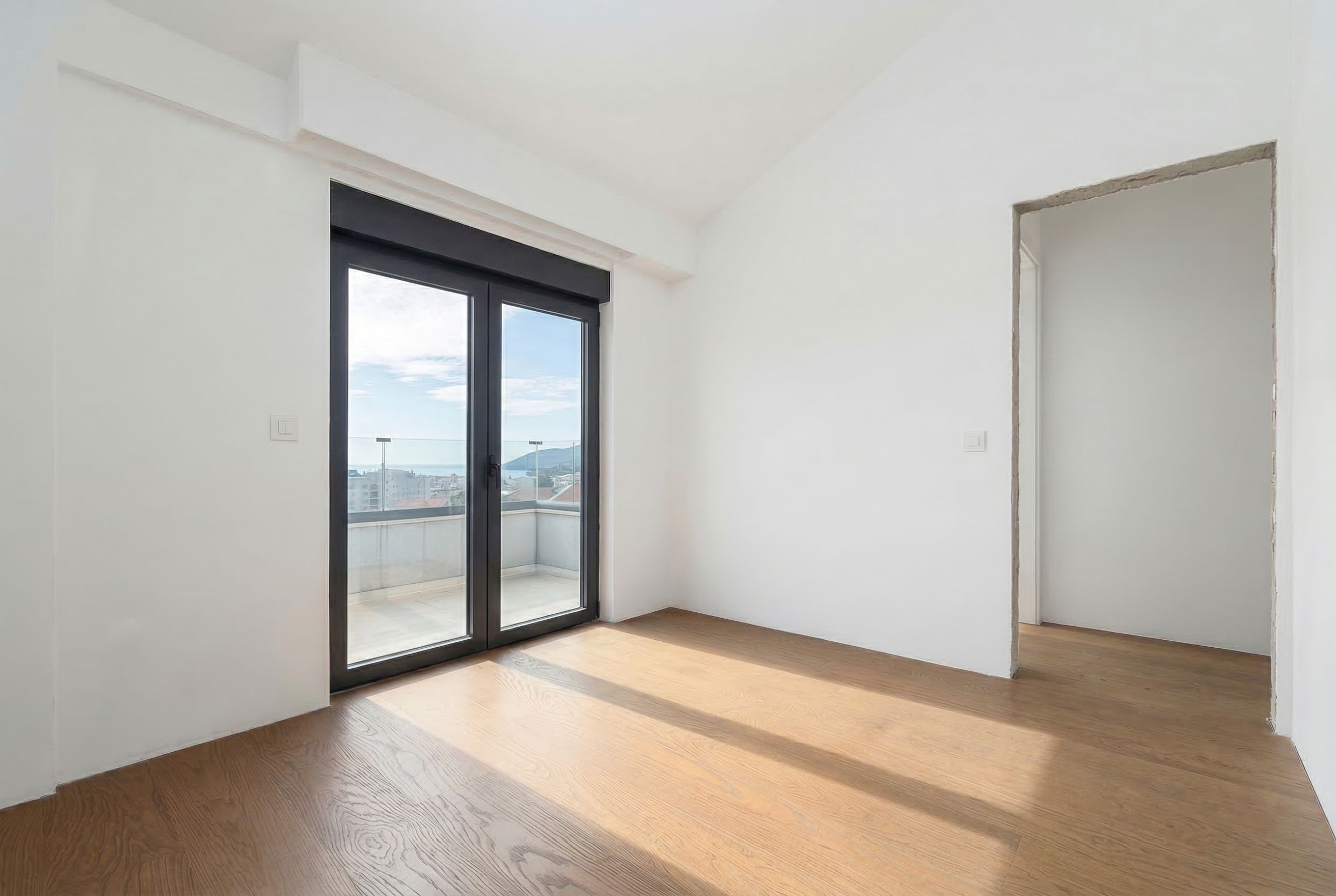 Bright bedroom in a penthouse in Budva, Montenegro: panoramic window, access to a balcony with a sea view, parquet flooring.