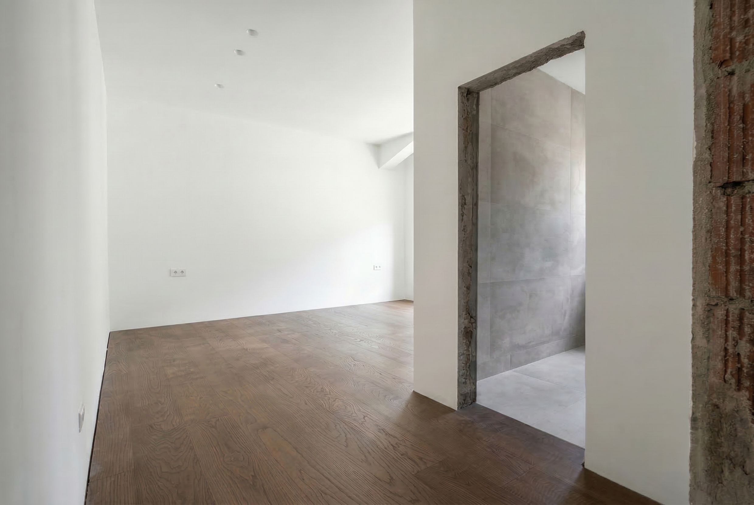 Living room interior in a penthouse in Budva, Montenegro: light-colored walls, wooden flooring, and an entrance to a tiled bathroom.