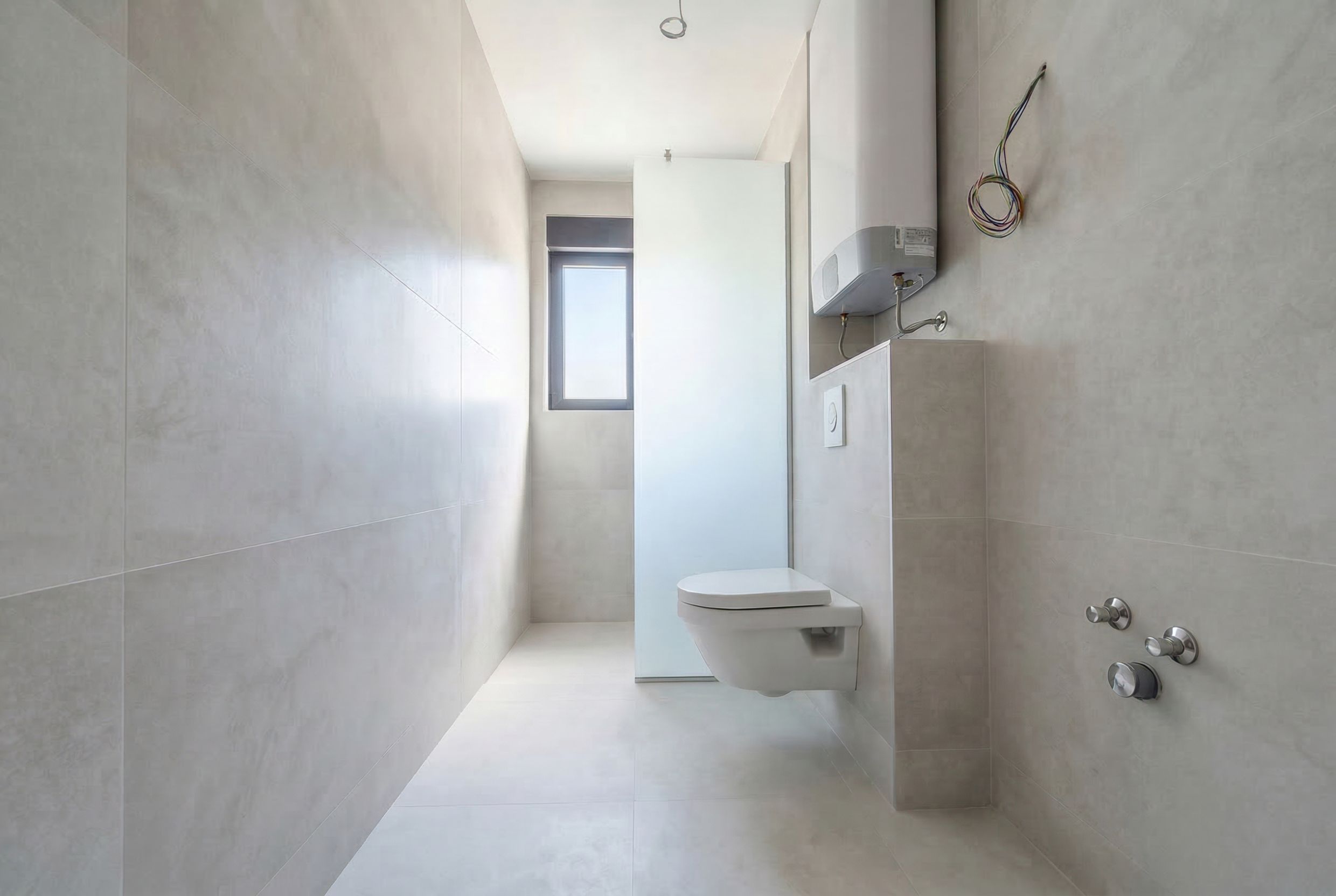 Modern bathroom in a penthouse in Budva, Montenegro: light-colored tiles, wall-hung toilet, and water heater.