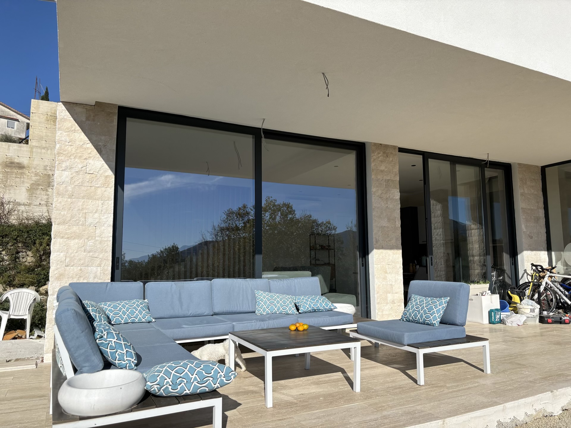 Terrace of a modern villa in Herceg Novi, Montenegro: blue upholstered furniture, panoramic glazing, and stone finishes.