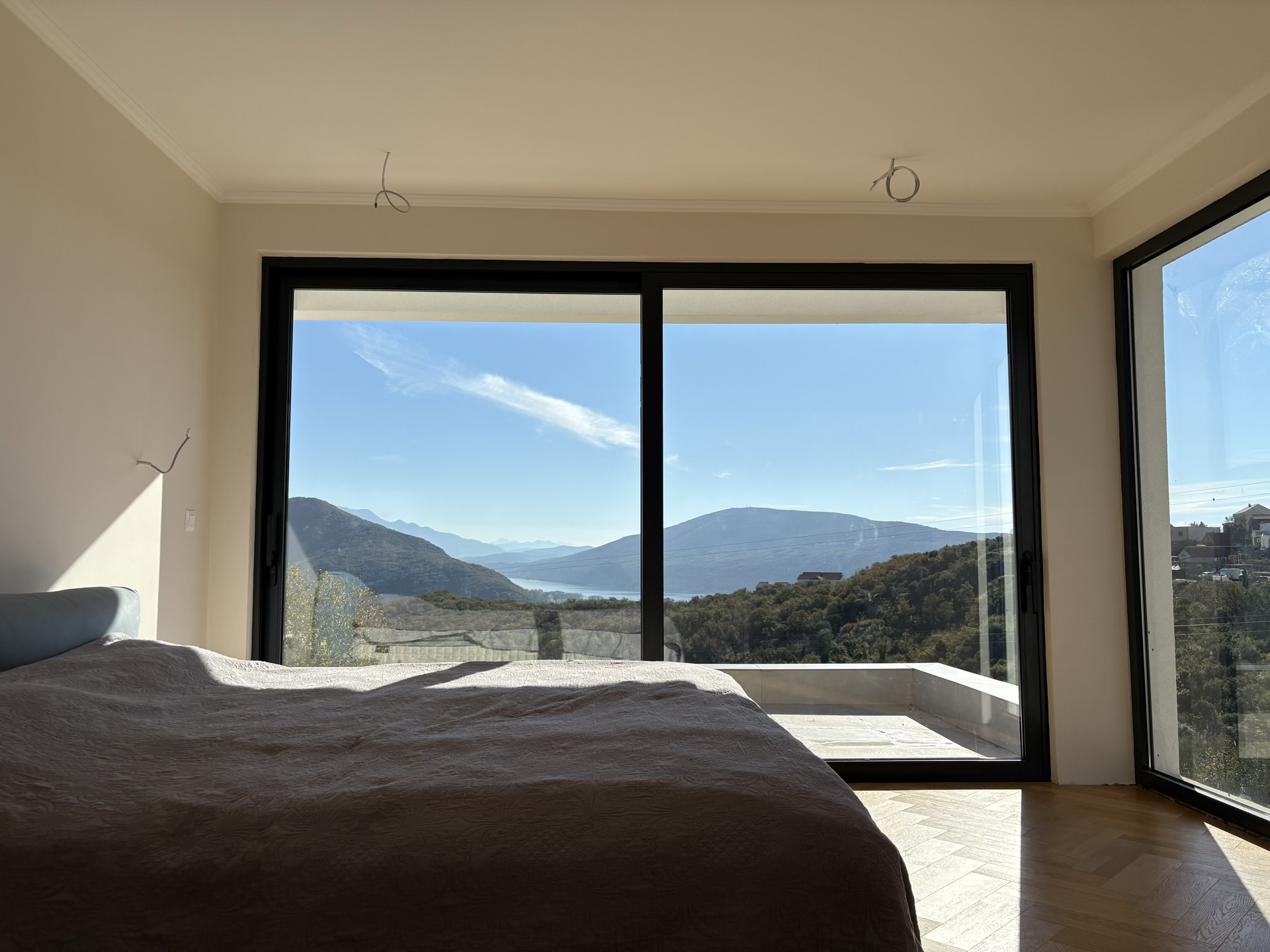 Bedroom in a villa in Herceg Novi, Montenegro: panoramic windows with mountain and sea views, parquet flooring, and a modern interior.