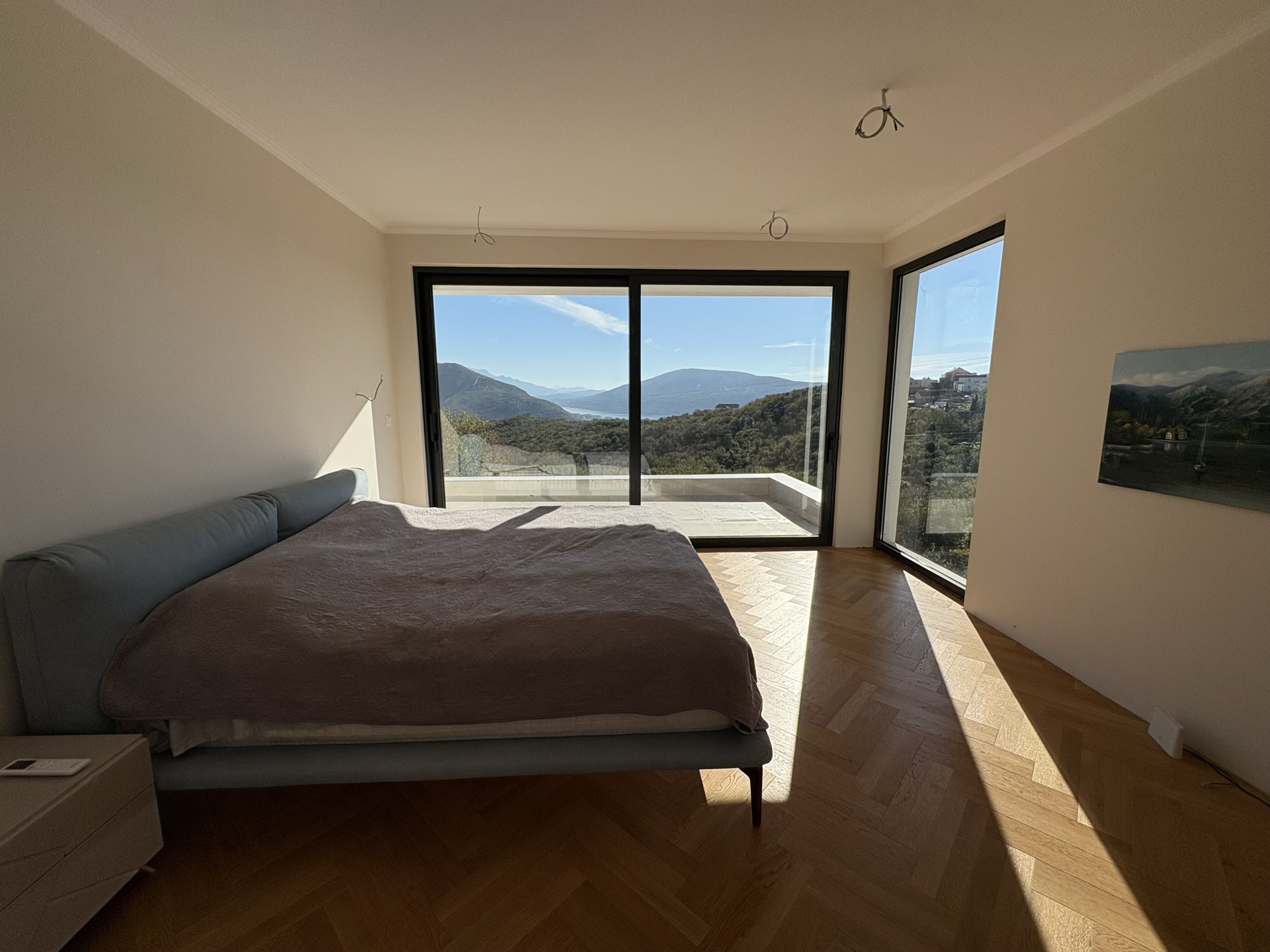 Bedroom in a villa in Herceg Novi, Montenegro: panoramic windows with mountain views, herringbone parquet, and modern furniture.