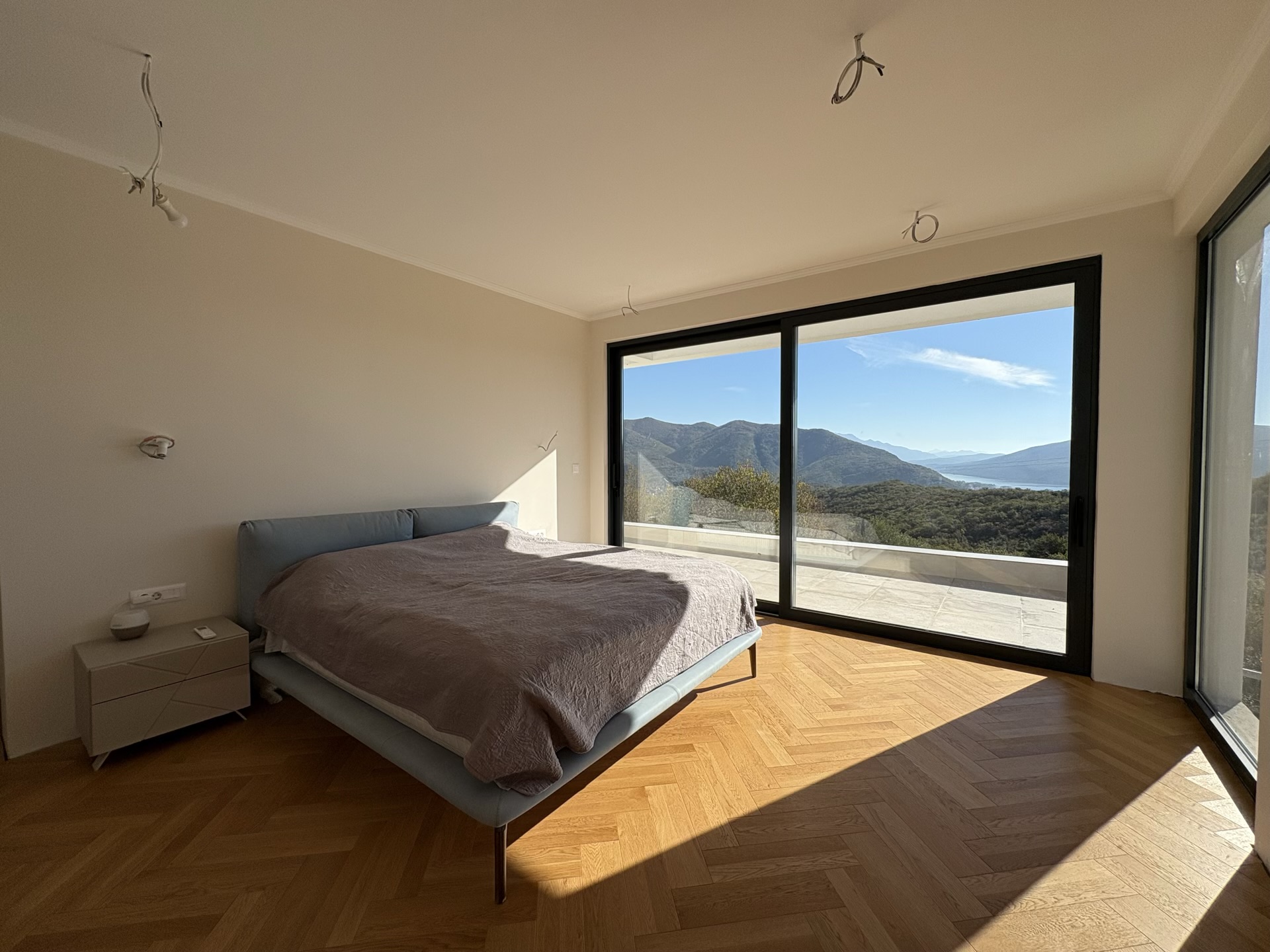 Bedroom in a villa in Herceg Novi, Montenegro: panoramic windows with mountain views, herringbone parquet, and a modern bed.