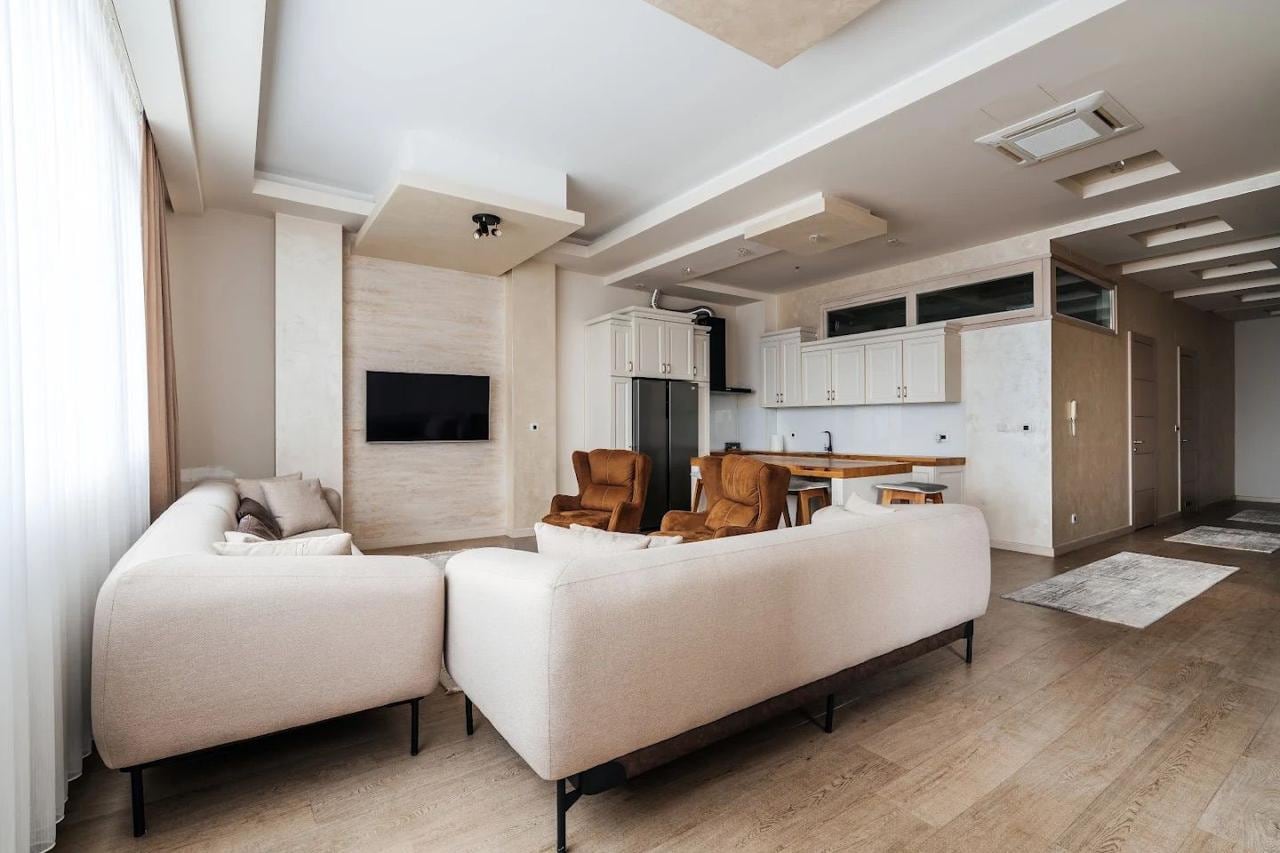 Modern living room with kitchen in an apartment in Budva, Montenegro: a light sofa, brown armchairs, and a stylish interior.