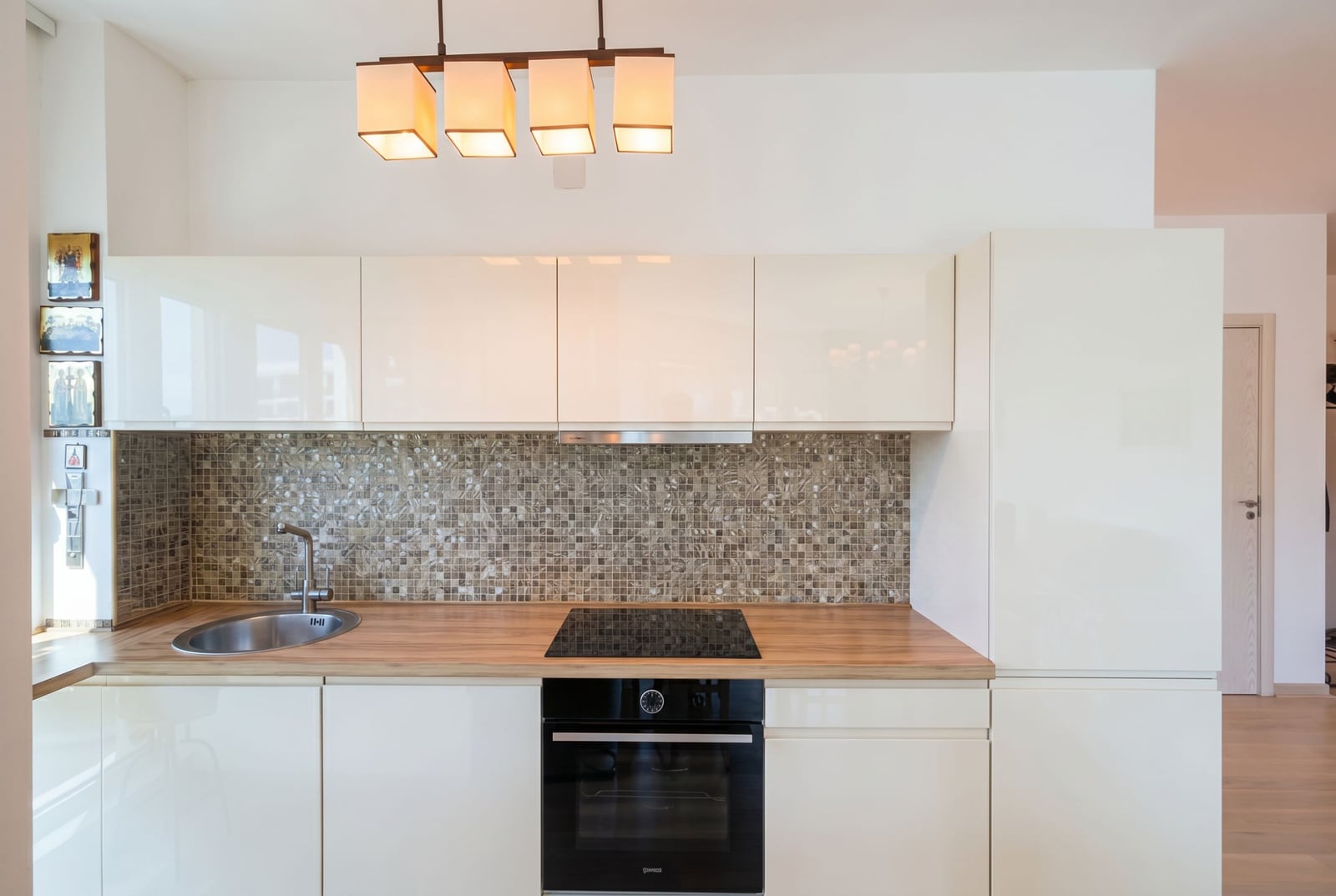 Modern white kitchen with a mosaic backsplash in an apartment in Bečići, Montenegro: built-in appliances and a wooden countertop.