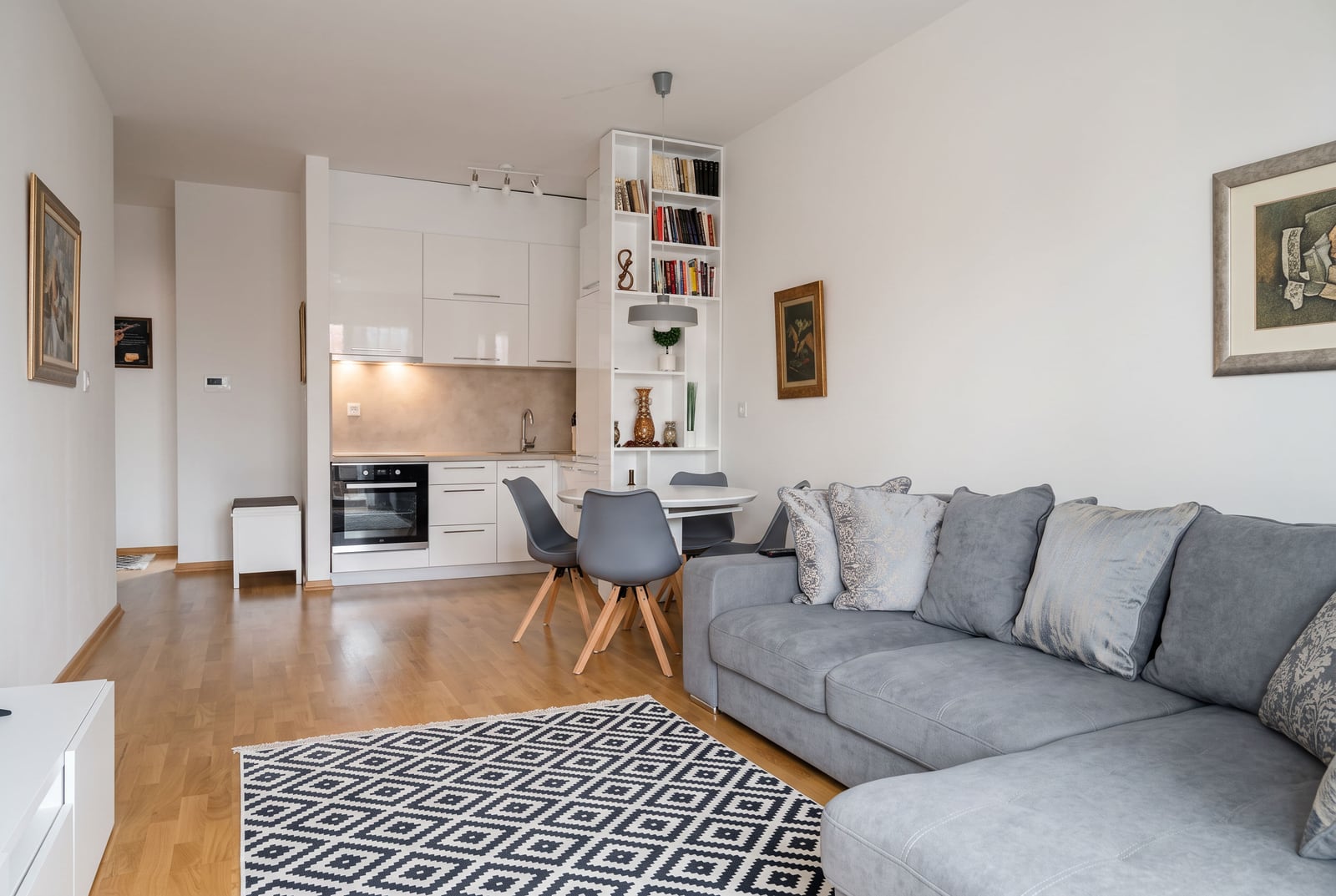Bright living room with a grey sofa, dining area, and open kitchen visible in the background.
