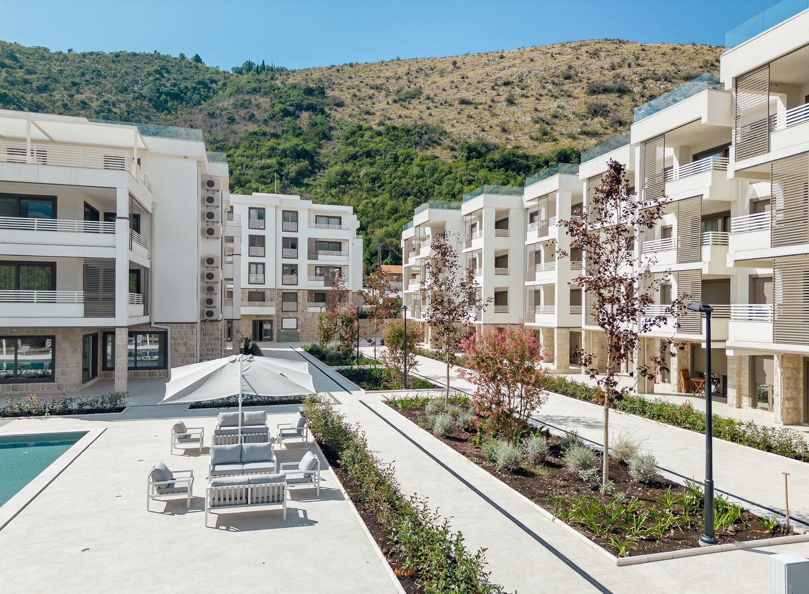 Modern residential complex in Igalo, Montenegro: landscaped area with a swimming pool, relaxation zone, and mountains.
